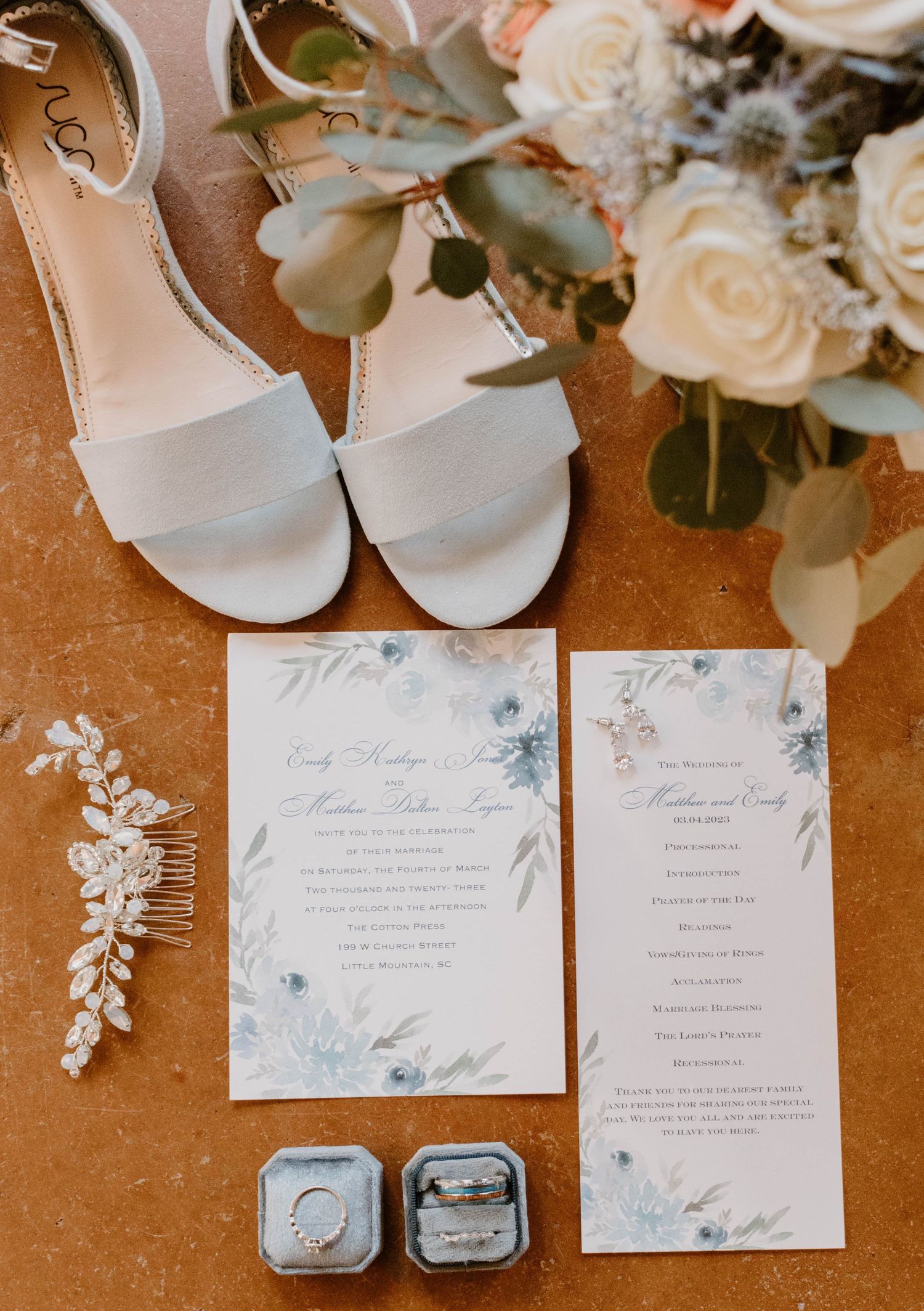 Wedding details flatlay with white sandals, floral invitations, and hair accessory.