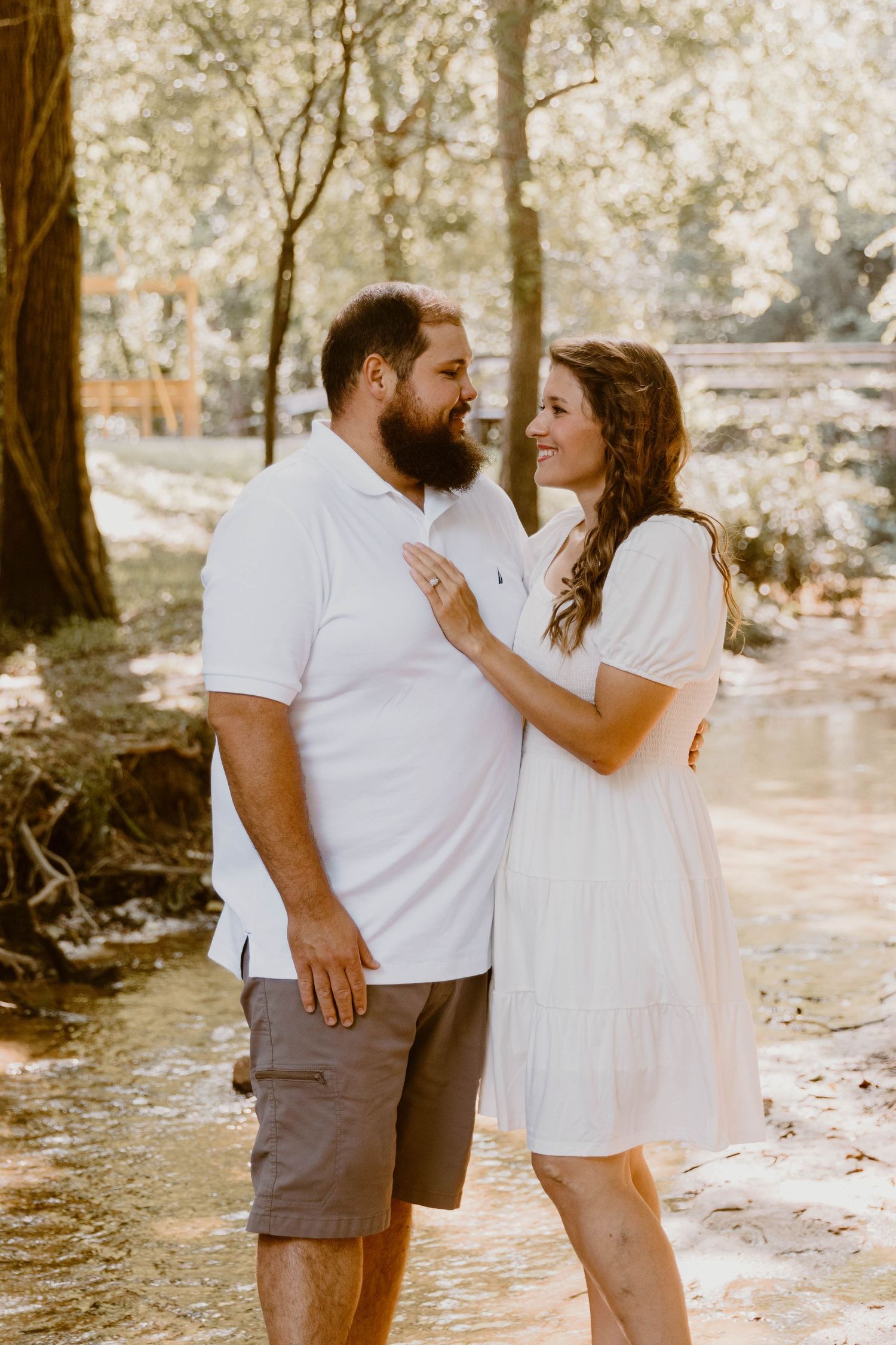A couple embraces while standing near a creek during their outdoor photo session.