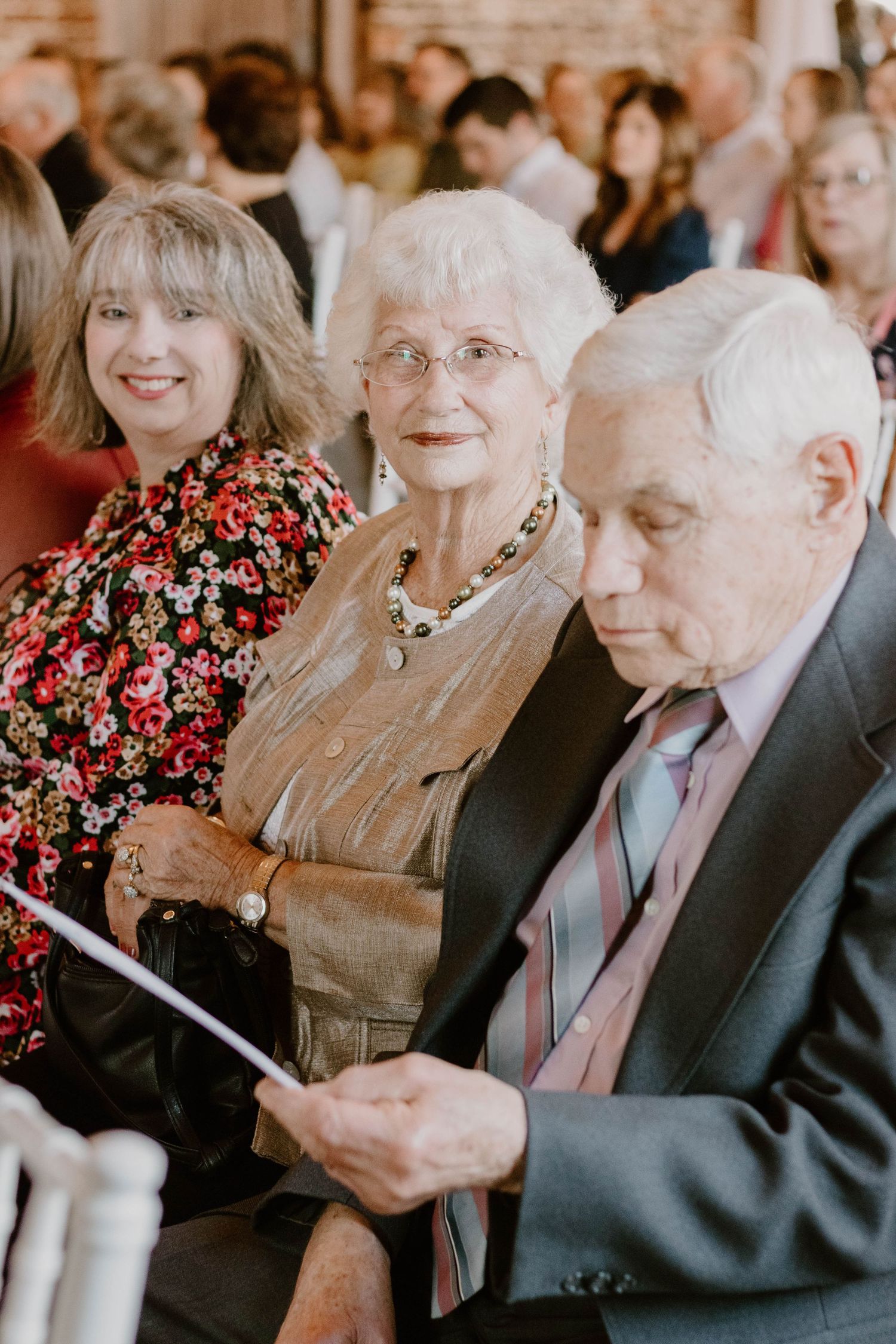 Wedding guests seated in rows during indoor ceremony with brick wall backdrop.