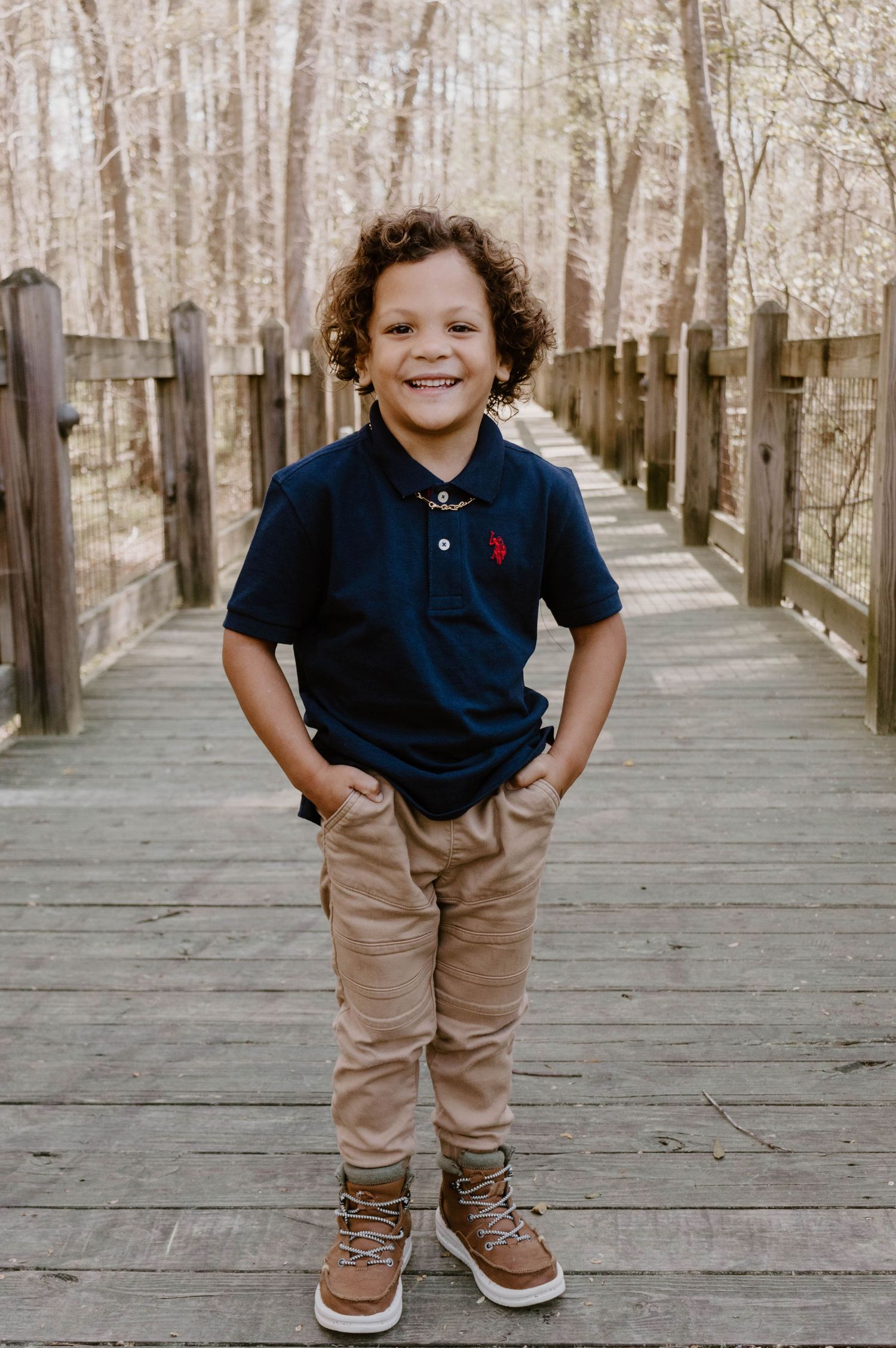A child in a navy polo and khaki pants stands confidently on a wooden boardwalk.