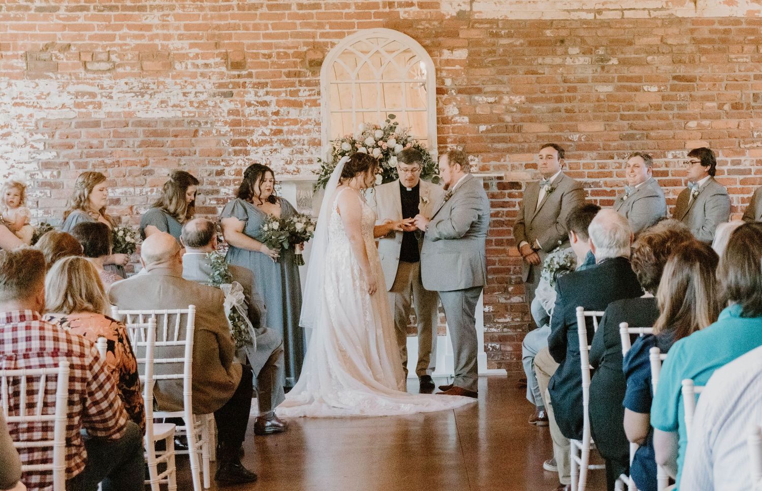 Wedding celebration in a rustic brick-walled venue with white chiavari chairs.