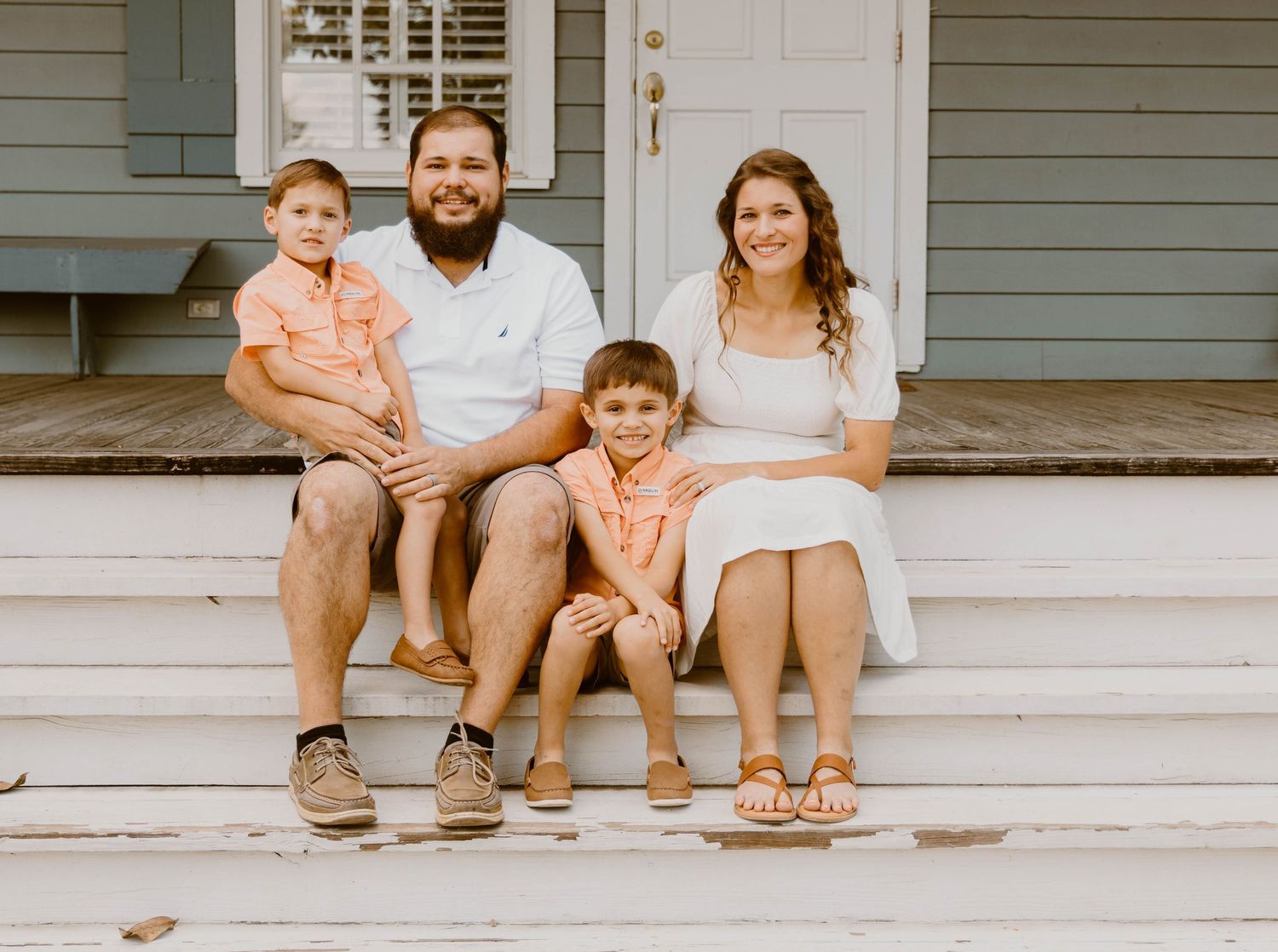 Family relaxing on front porch steps of gray house with white door and shutters.