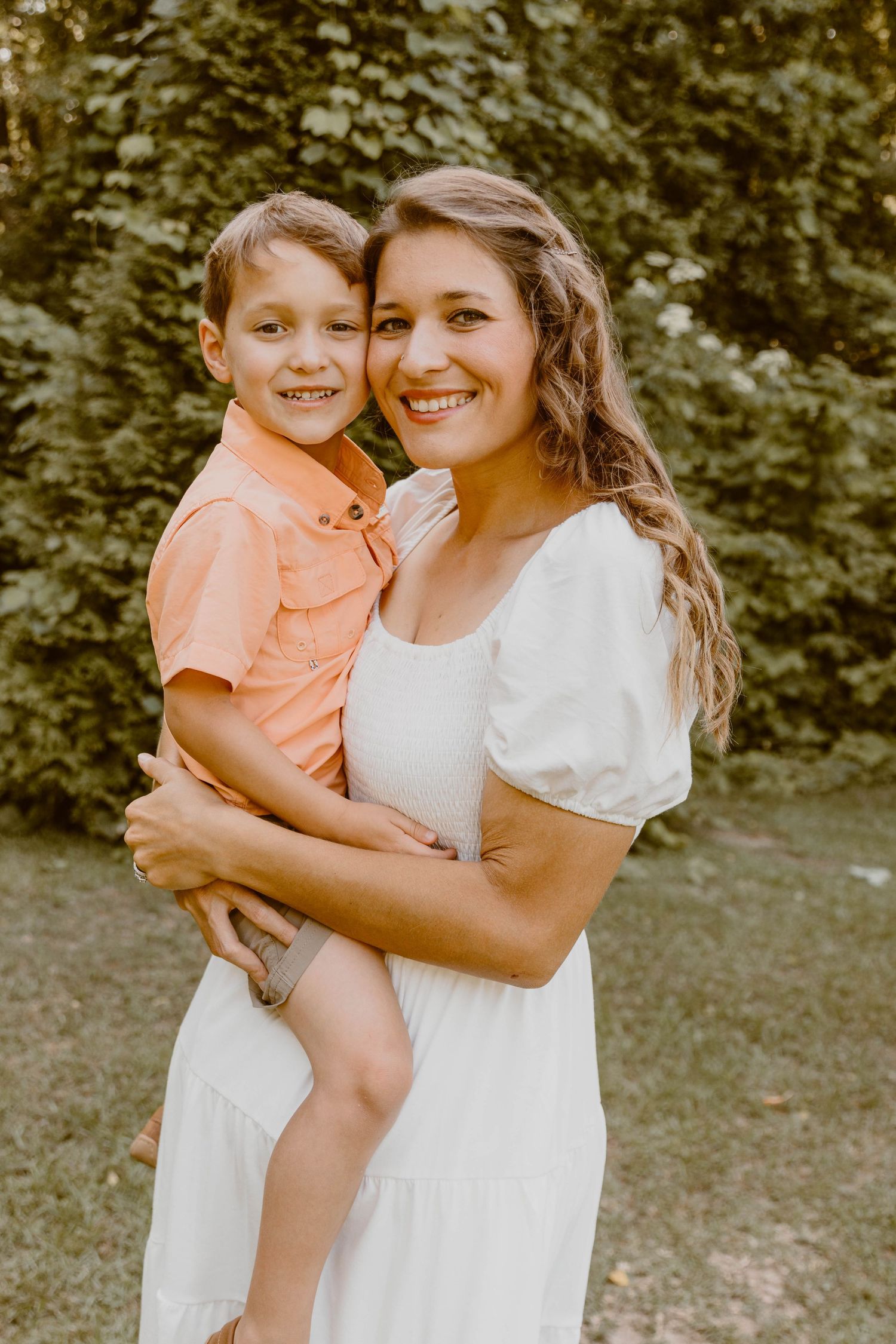 Mother and child embracing while wearing white and peach outfits outdoors.