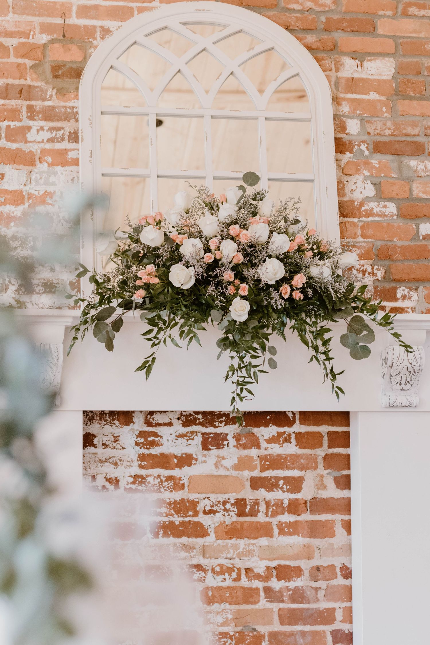 Romantic floral arrangement with pink roses and greenery against white arched window frame.