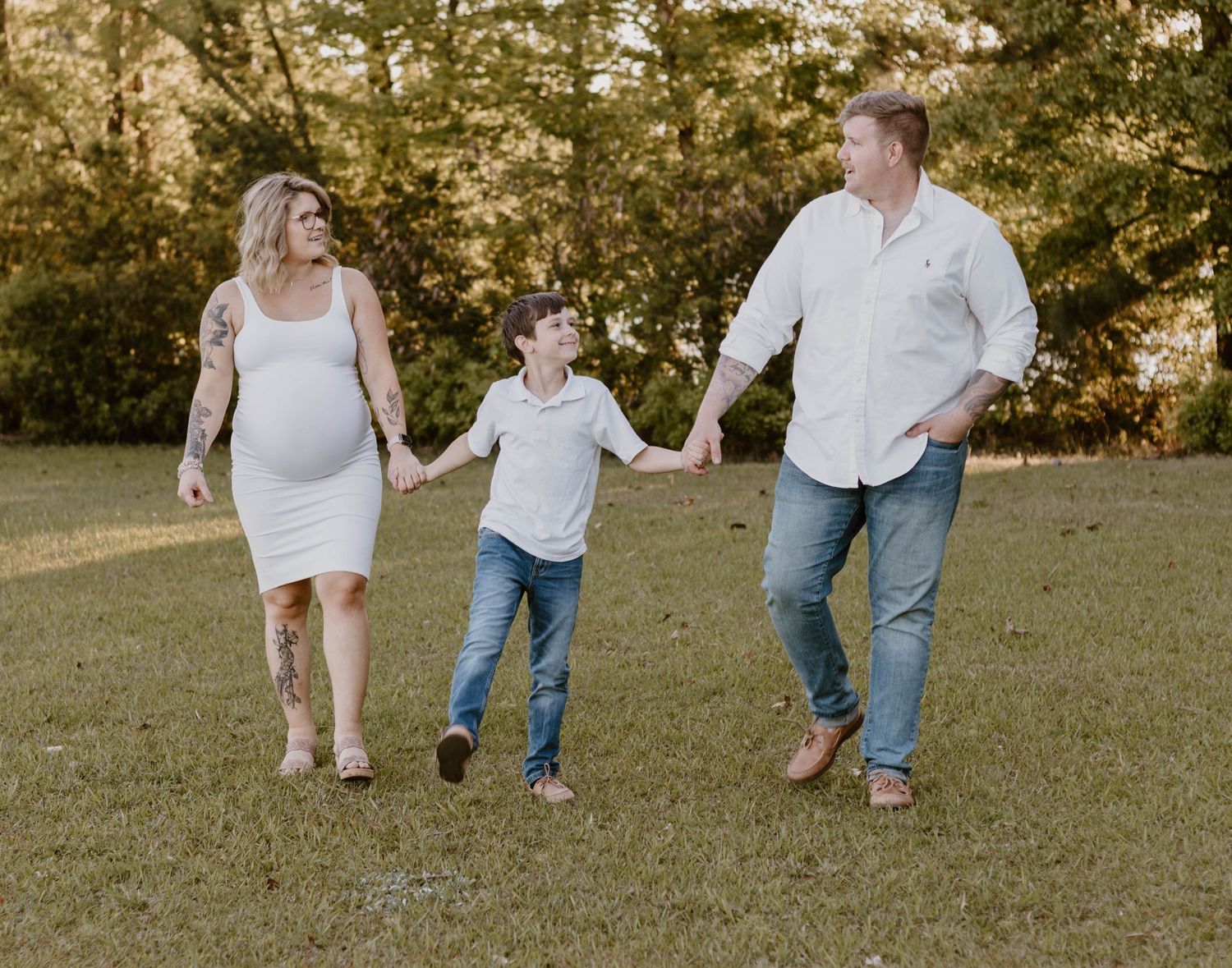 Three people walk hand in hand through a grassy field during a sunset photoshoot.