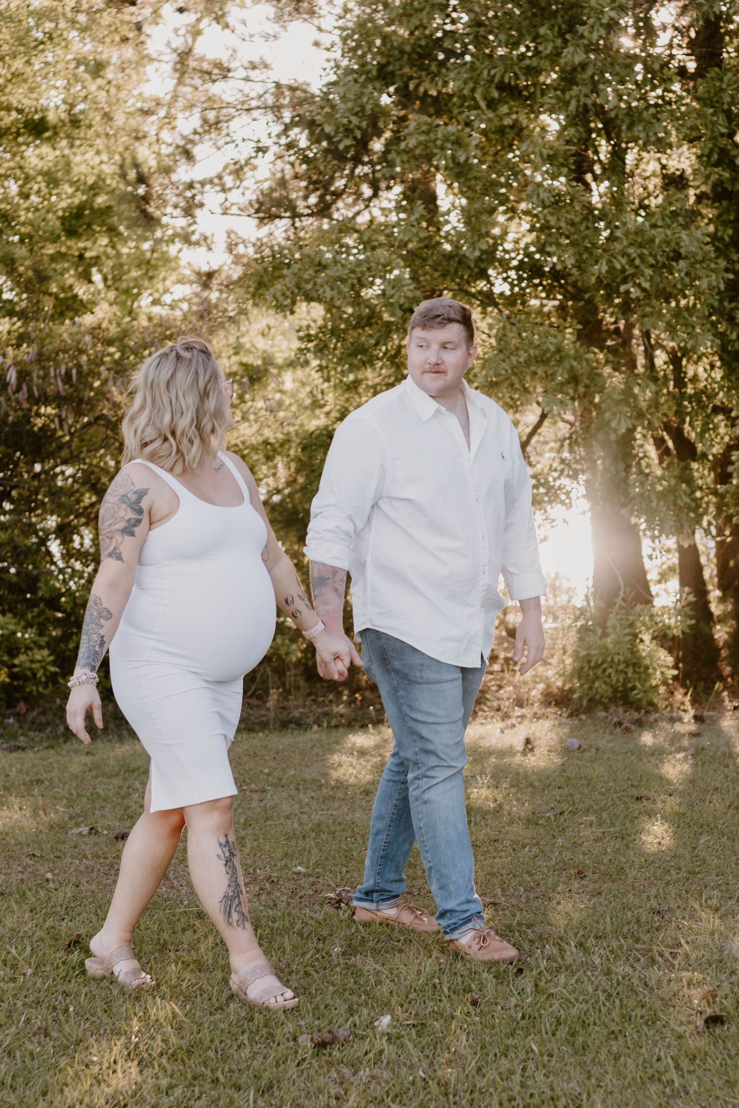 A couple walks hand in hand during their outdoor maternity photo session at golden hour.