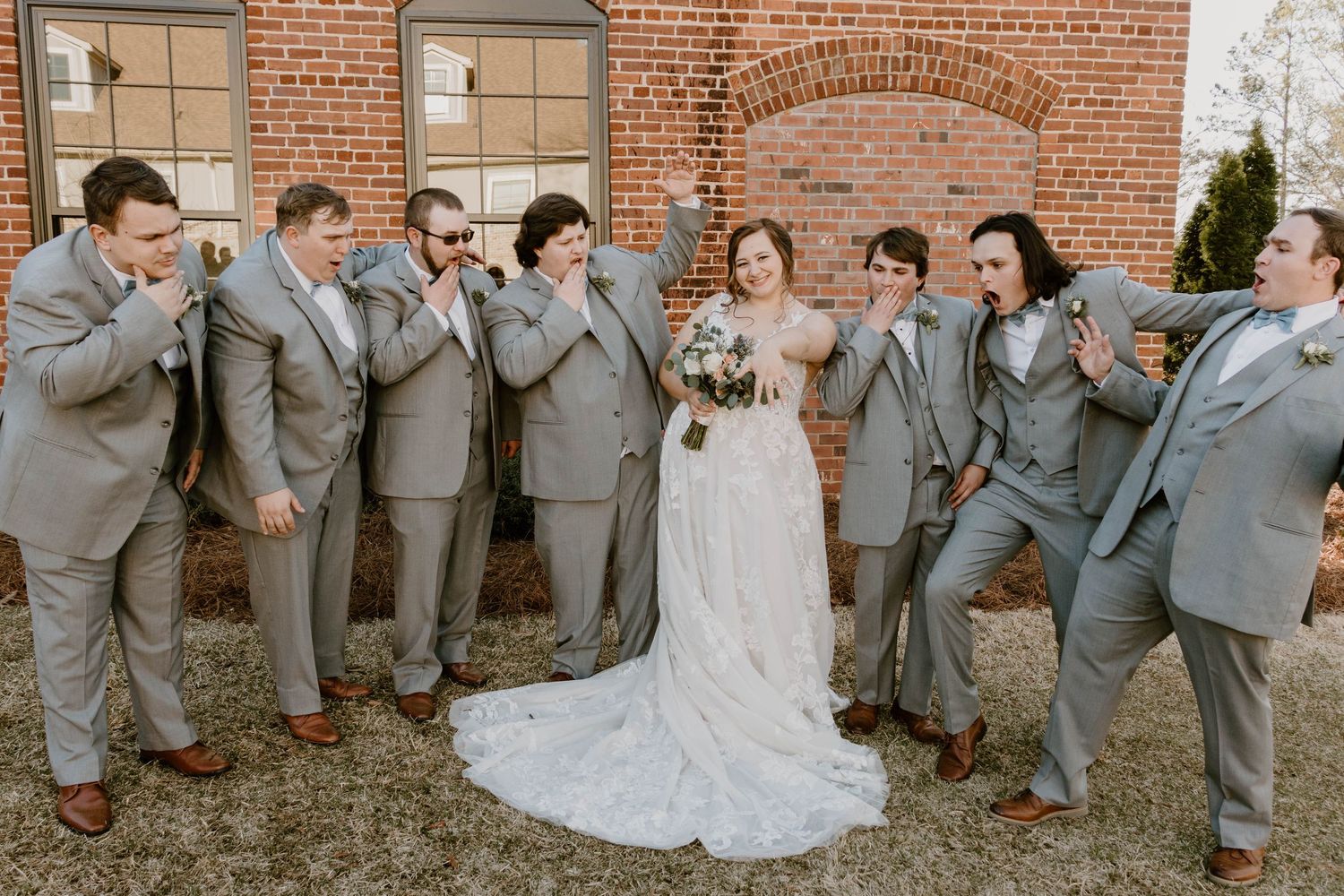 Wedding party poses for candid shots against brick exterior in grey and blue color scheme.