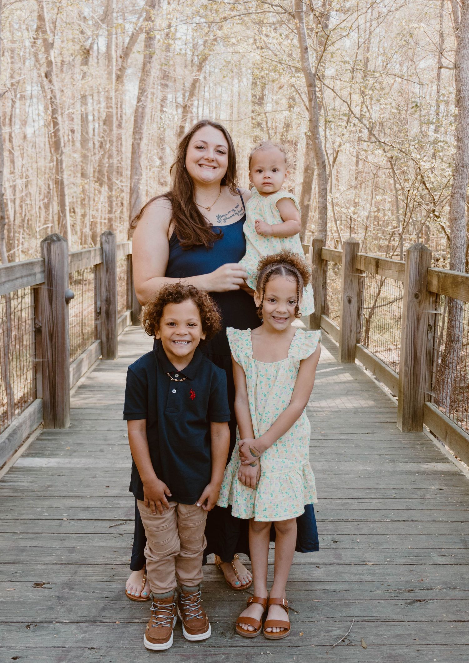 A family group stands together smiling on an elevated wooden path through a forest.