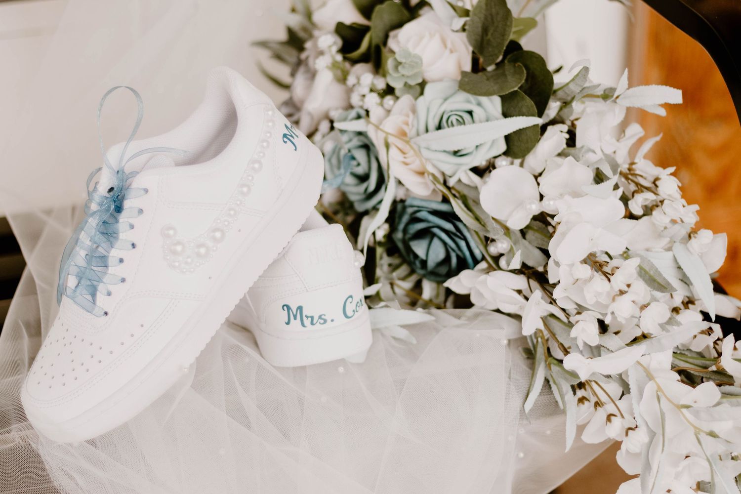 White bridal sneakers and delicate blue and white floral bouquet arranged for wedding detail shot.