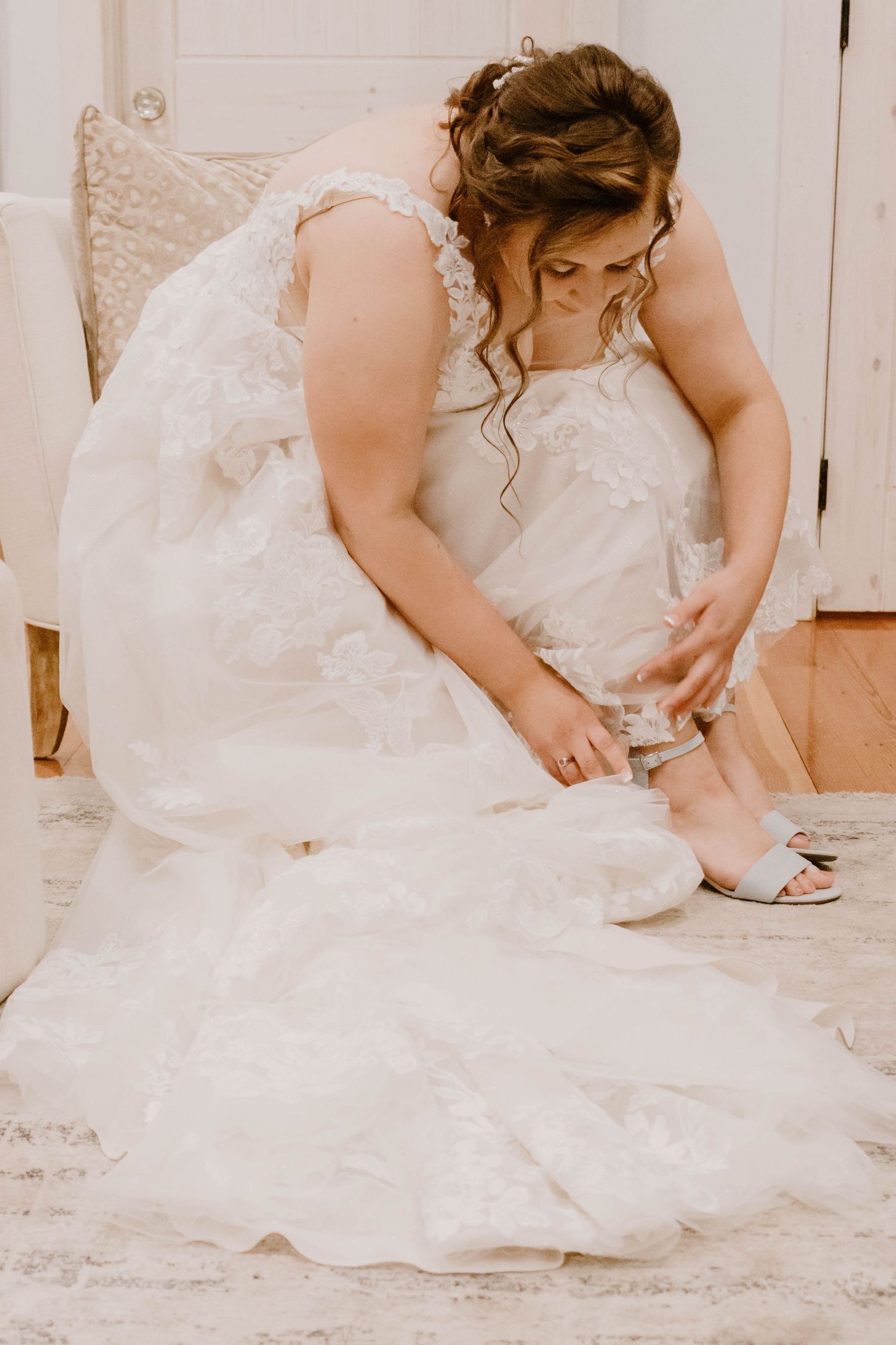 Wedding dress detail shot showing intricate lace patterns and beading on a hardwood floor.