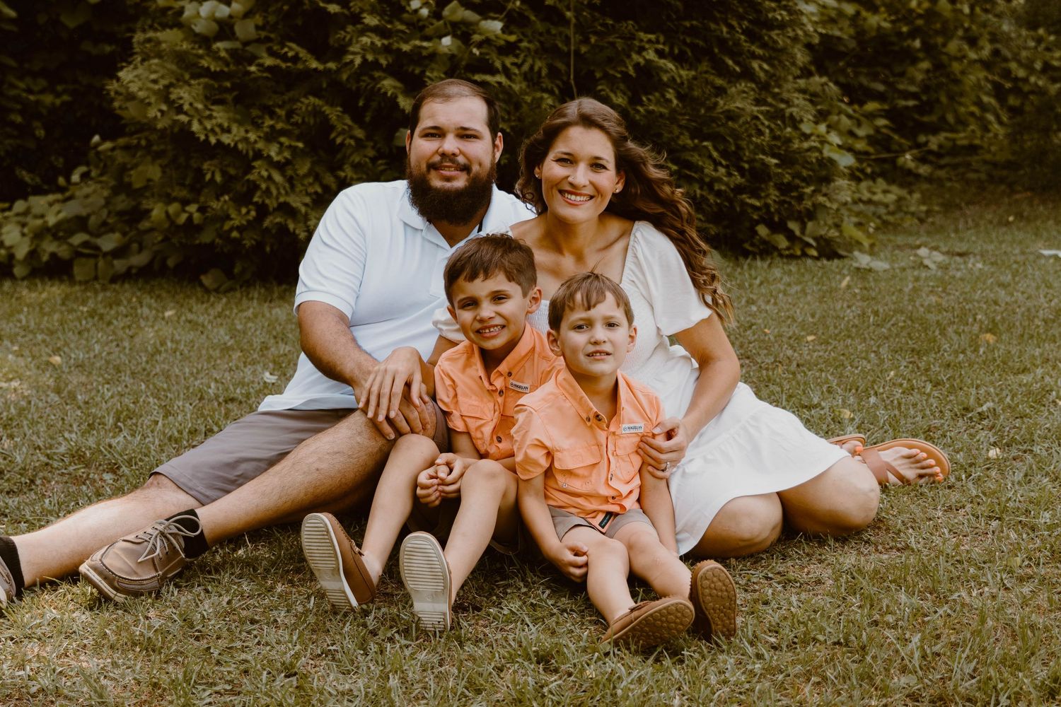 Family relaxing together on grass during outdoor photo session.