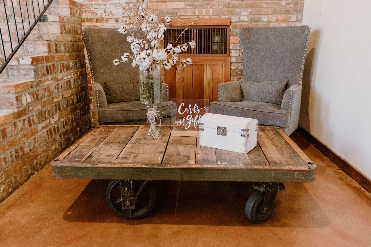 Industrial chic coffee table with wheels and gray armchairs against exposed brick wall.