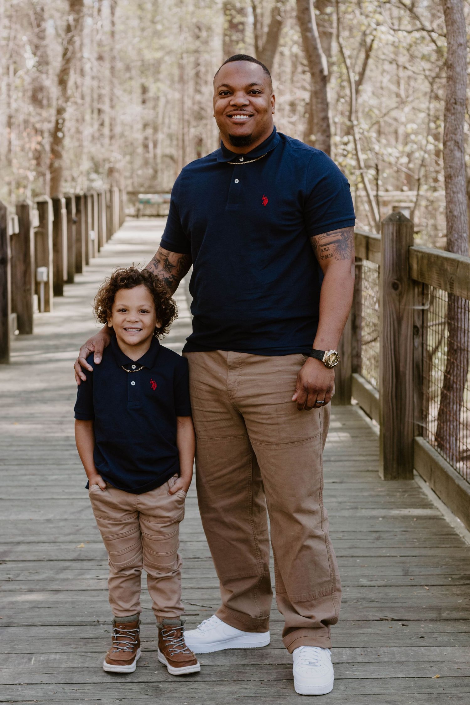 Two people in matching navy polos and khakis stand together on a wooden walkway.