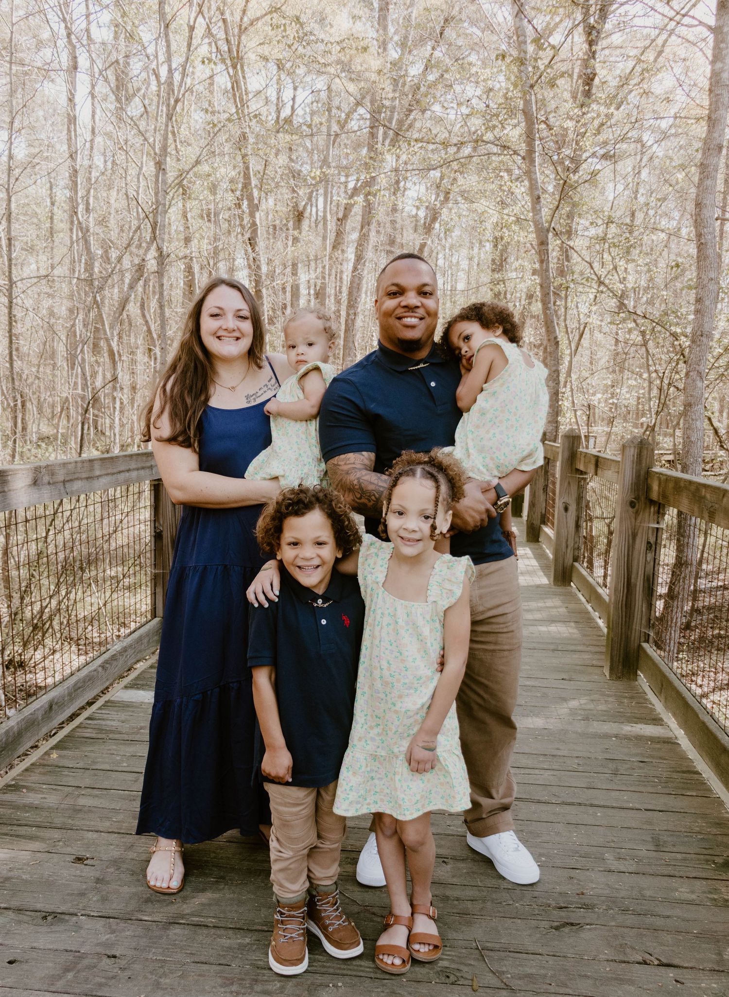 A joyful family poses together on an elevated wooden walkway surrounded by trees.