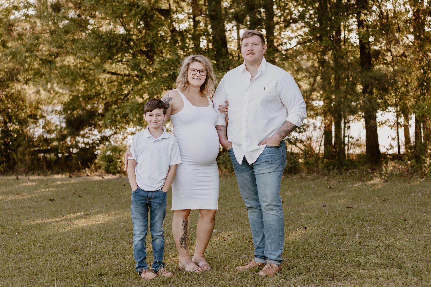 Family portrait in casual attire against wooded background during golden hour.