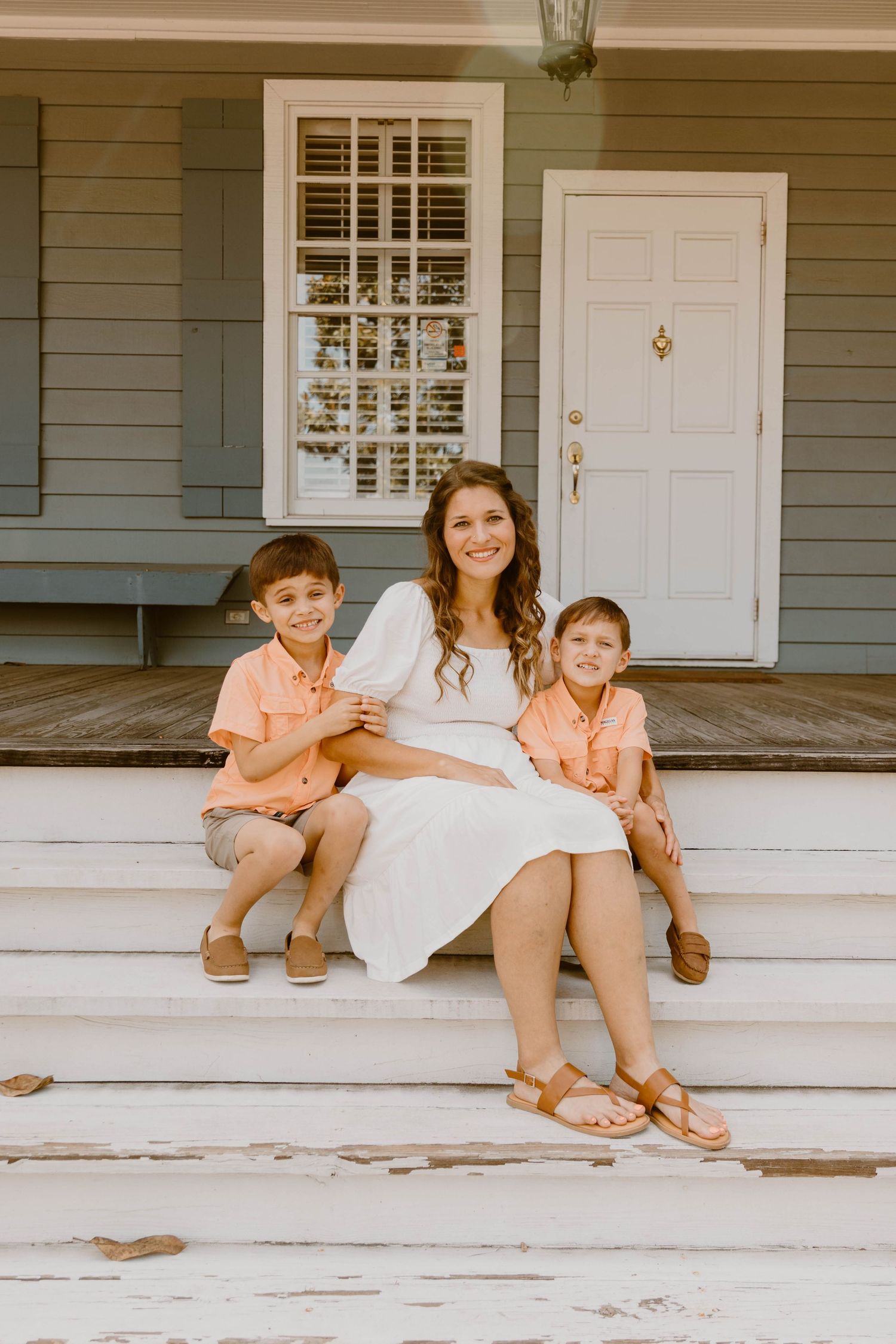 Family sitting together on rustic white porch steps in summer attire.