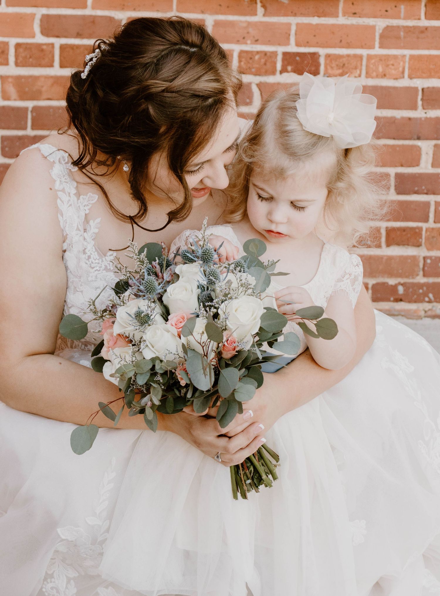 Elegant wedding bouquets with white flowers and eucalyptus leaves held against white dress.