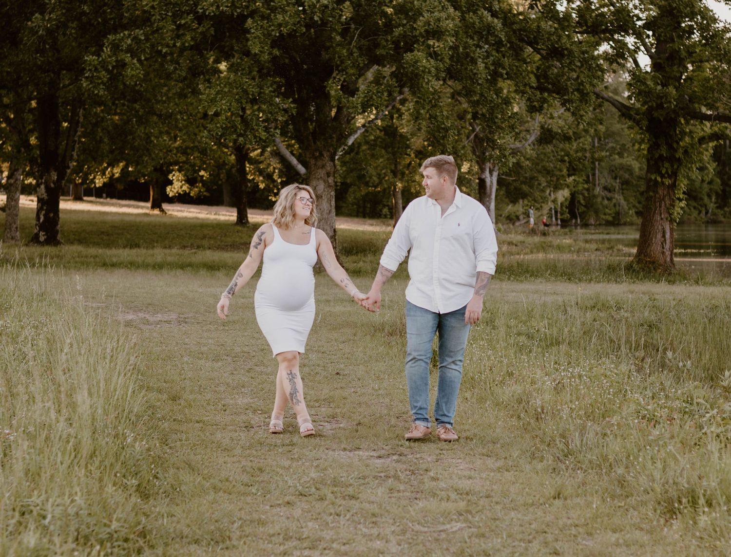 A couple holds hands while walking through a serene park setting during golden hour.
