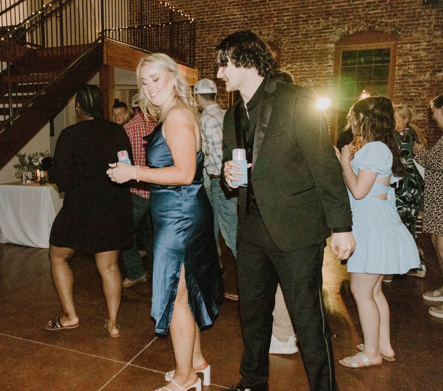 Guests mingling and dancing at a wedding reception in a rustic brick venue.