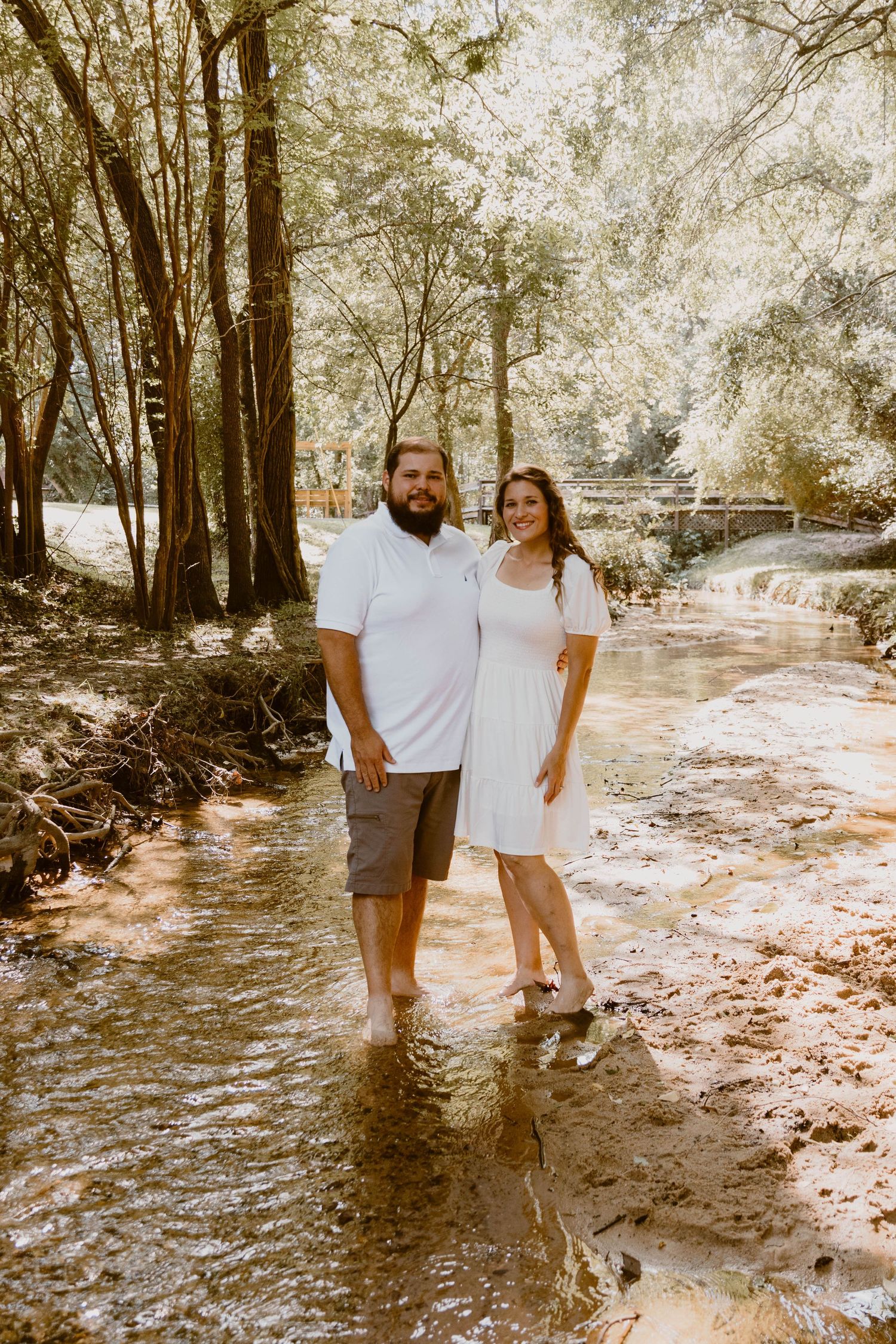 A couple shares intimate moments while standing in shallow water during a forest photoshoot.