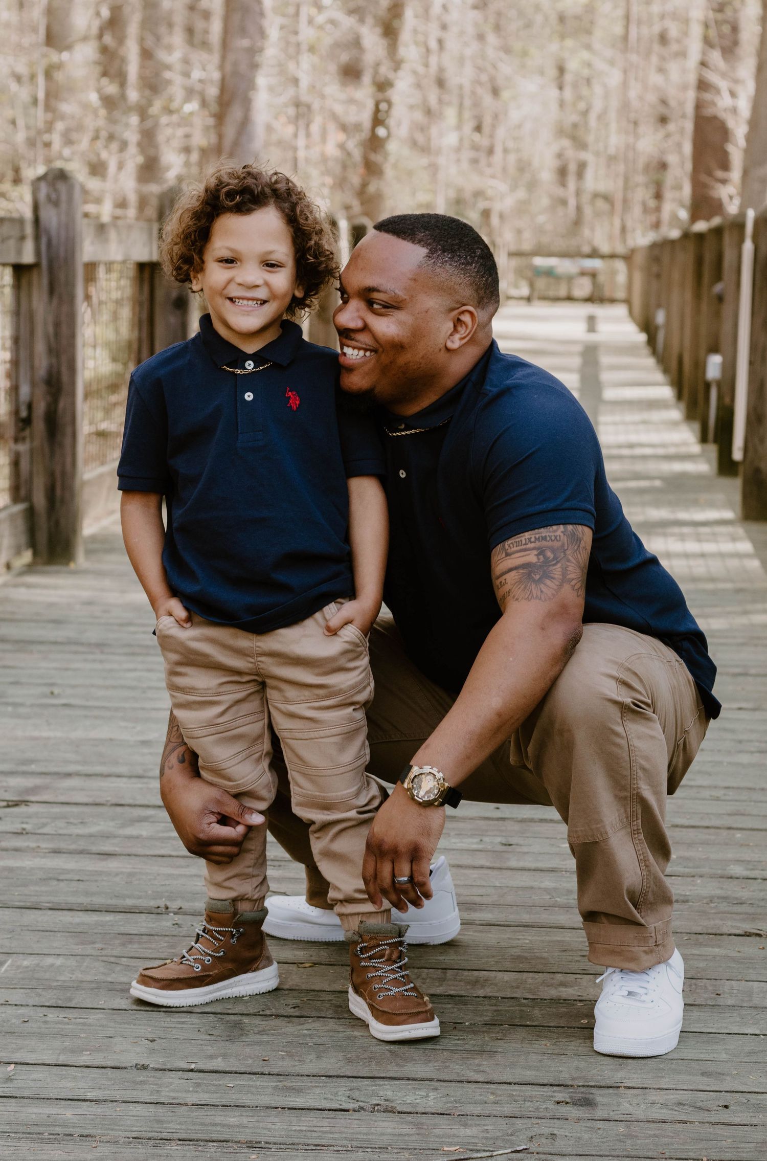 Family photo session on a wooden boardwalk showing playful interactions in coordinated navy and khaki outfits.