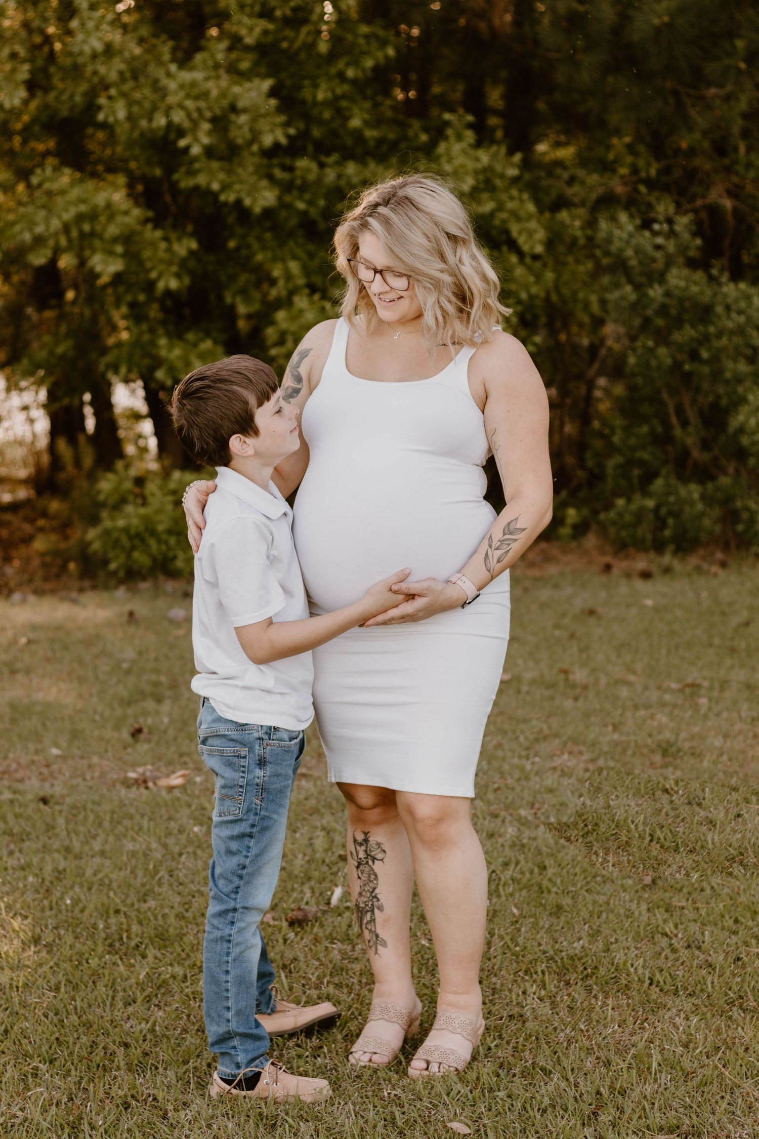 A tender moment between mother and child as they embrace her pregnant belly outdoors.