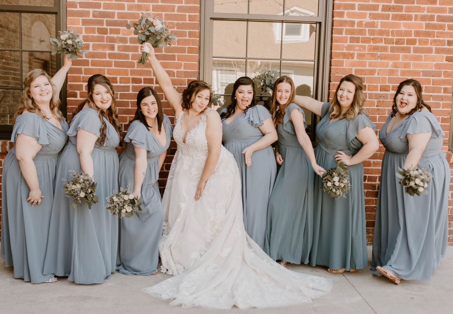 Bridesmaids in coordinated slate blue dresses arranged in line formation.