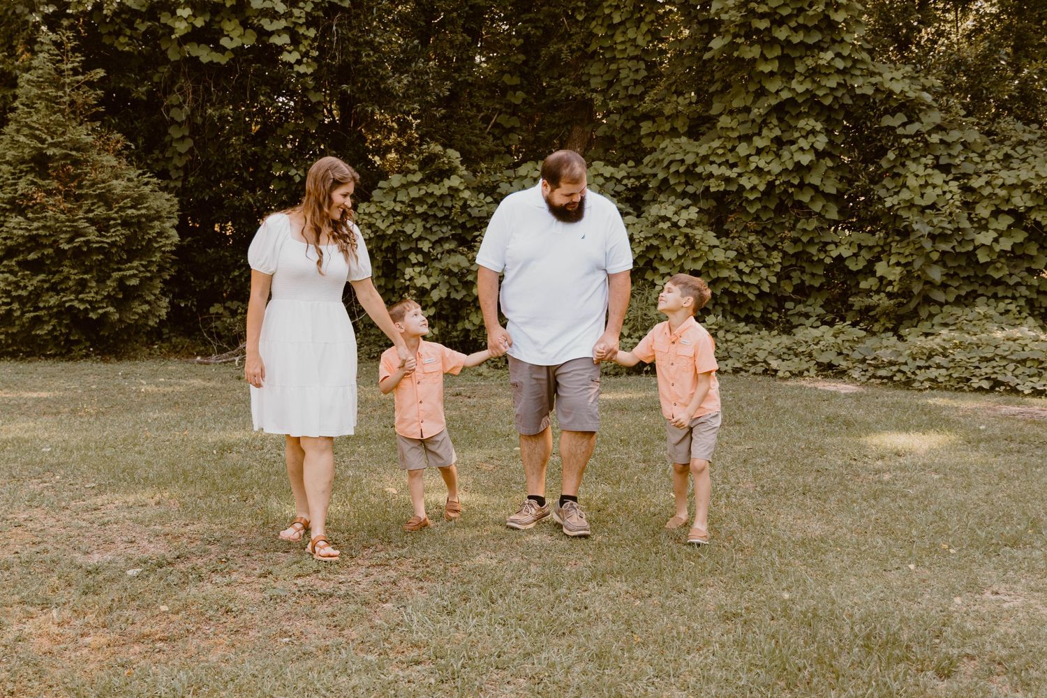 Family walking together in a grassy outdoor area wearing coordinated peach and white outfits.