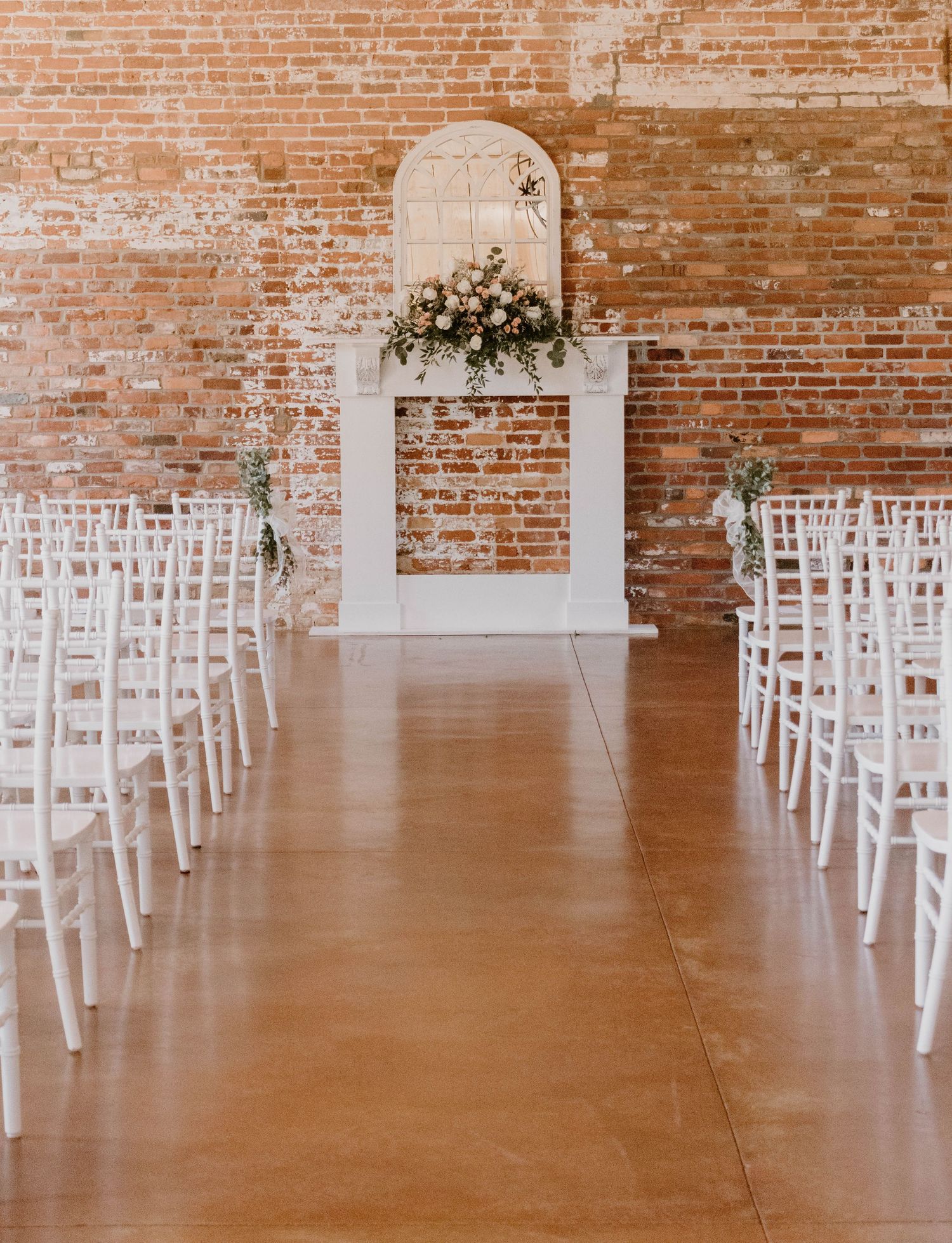 White chairs arranged in rows for a wedding ceremony in an industrial brick venue.