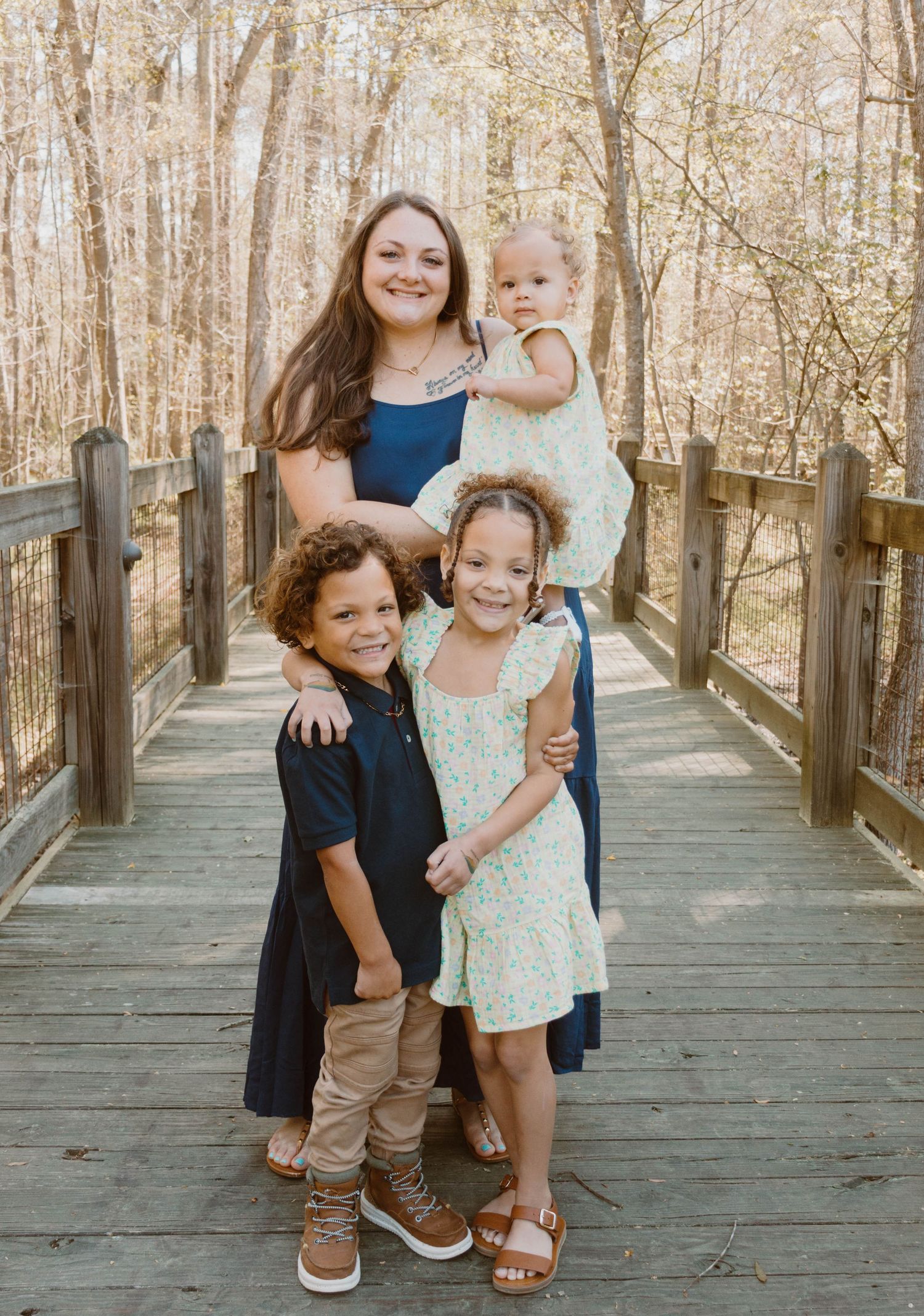 A happy family of four poses together on a wooden boardwalk surrounded by autumn trees.