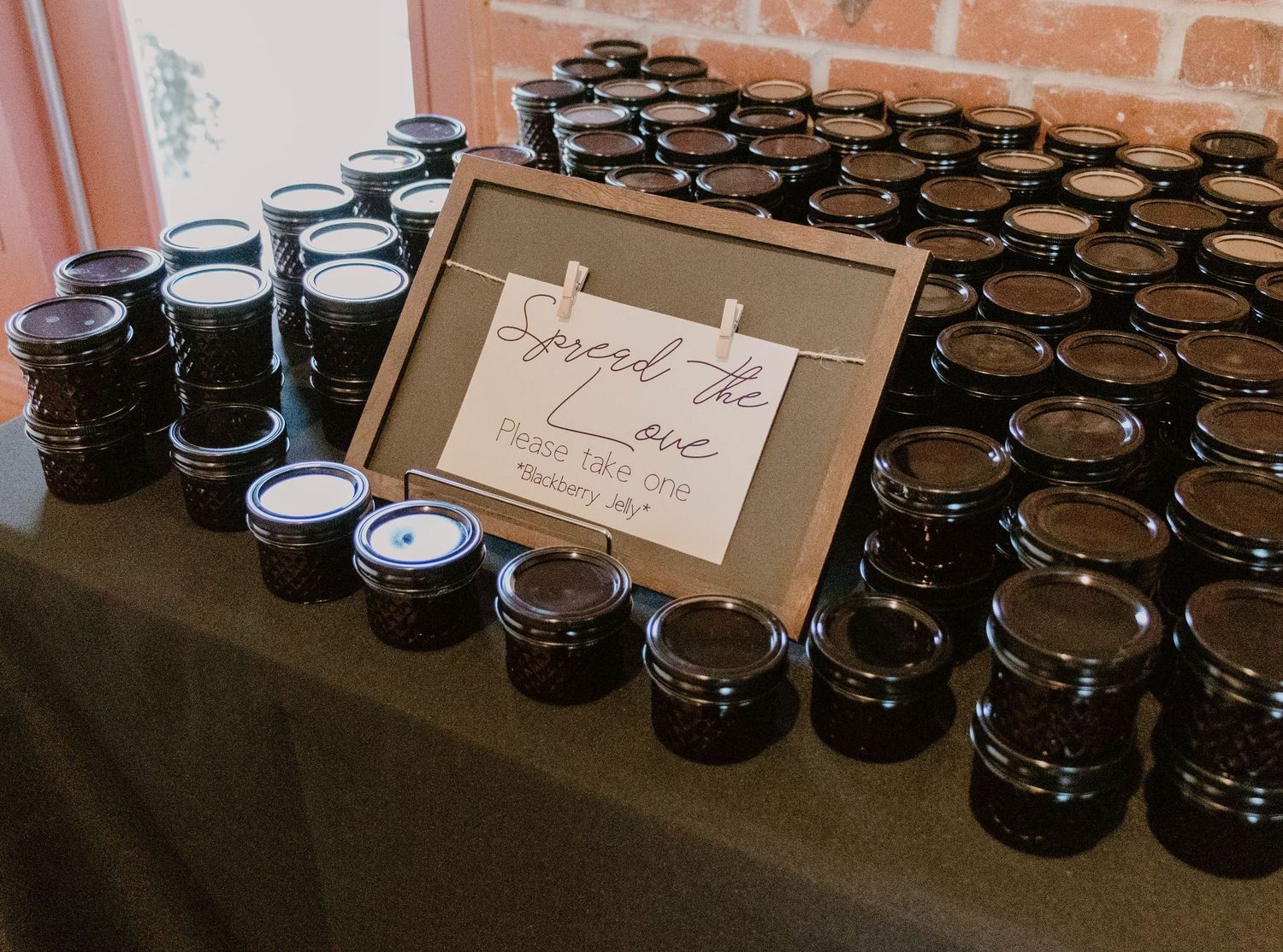 Display table with rows of small mason jars and a framed sign for wedding favors.