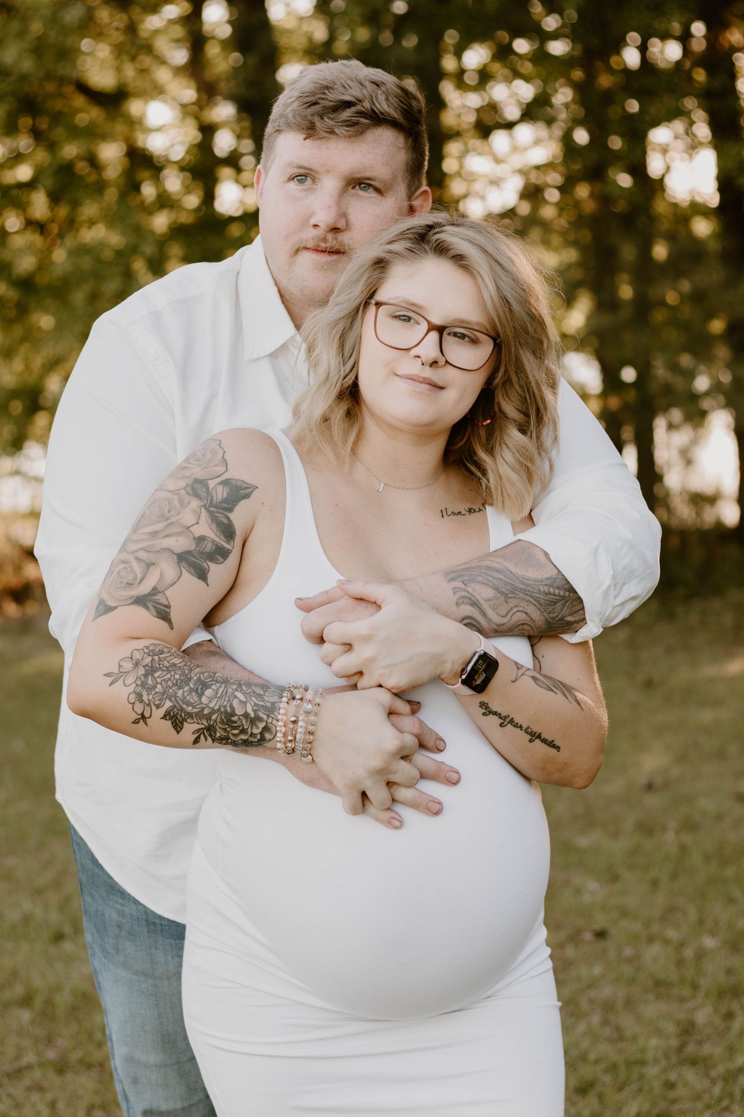 A couple shares an embrace during their outdoor maternity photoshoot in warm evening light.