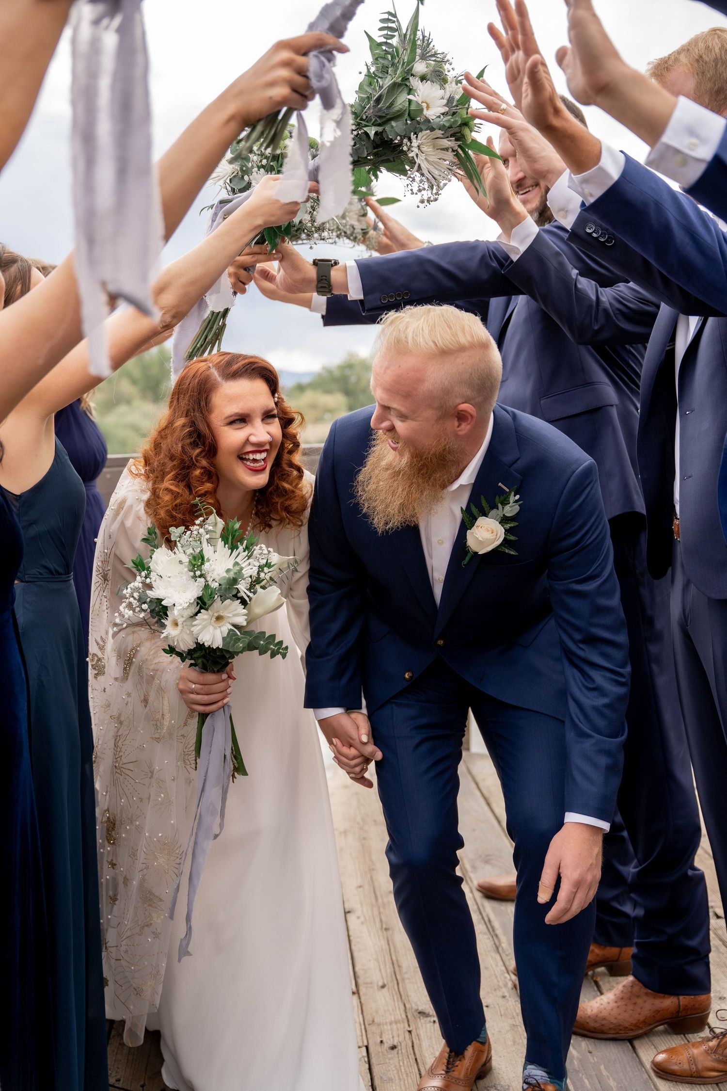 A joyful wedding couple shares a candid moment while their wedding party raises hands in celebration around them.
