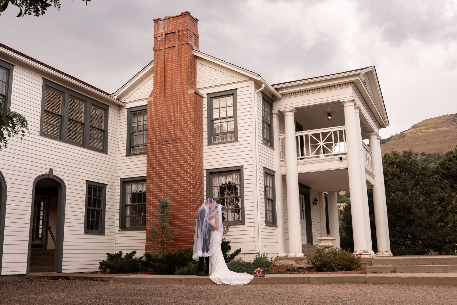 Classic white colonial mansion with tall brick chimney and wedding couple in foreground.