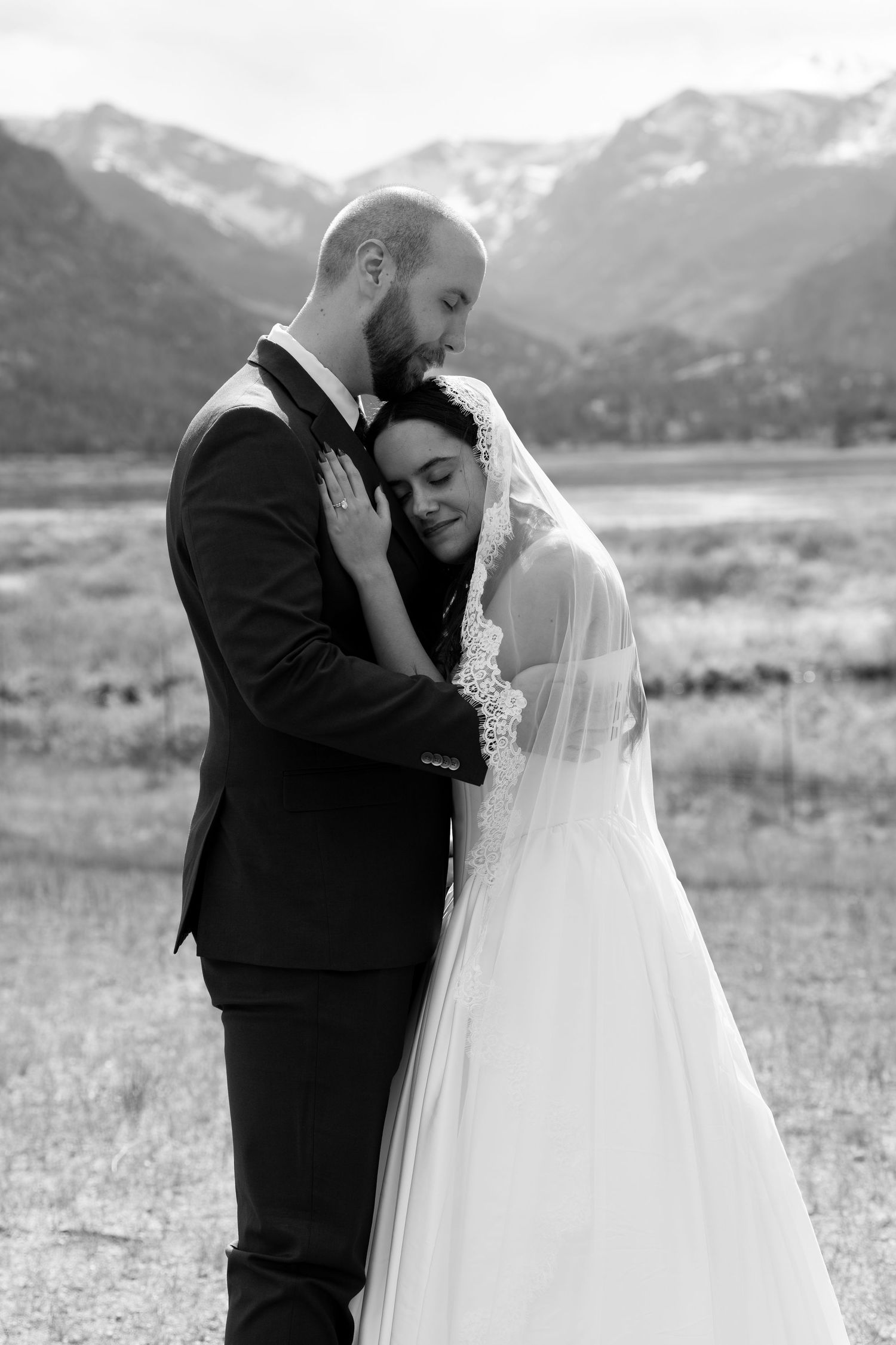 Black and white photo of bride and groom embracing with Rocky Mountain backdrop on their wedding day.