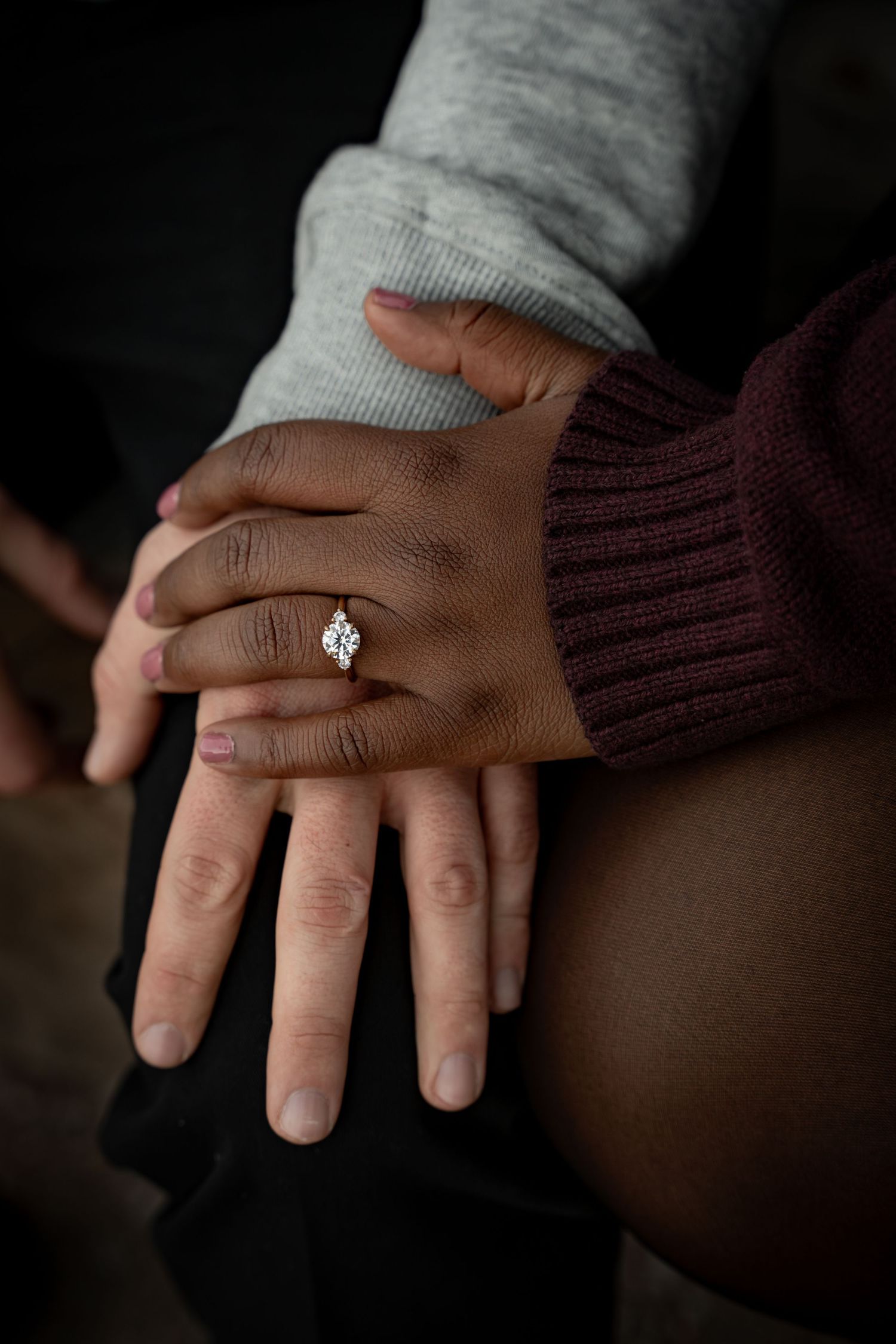 Close-up of an interracial couple holding hands, showcasing a diamond engagement ring on the woman's finger.