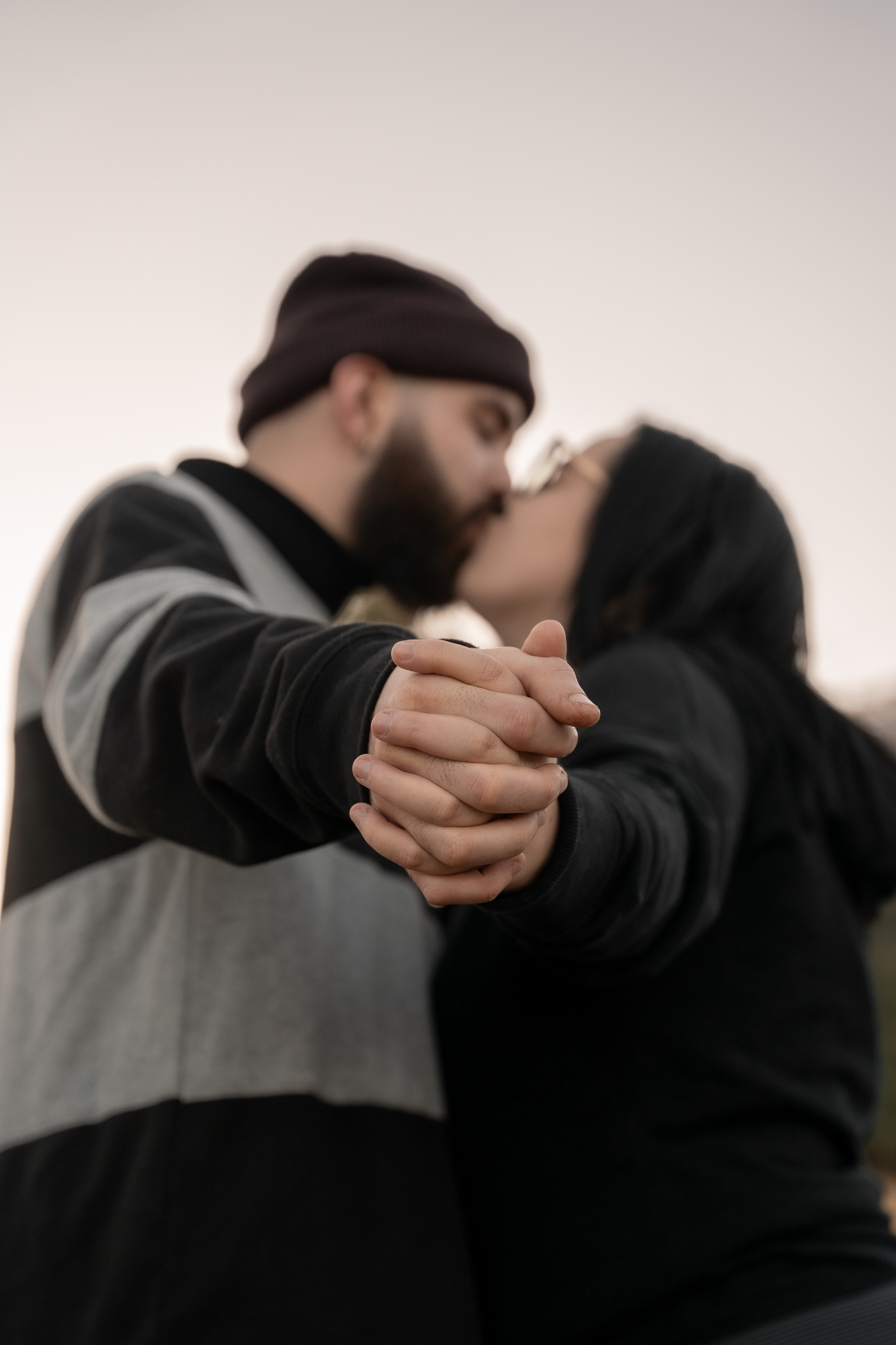 A romantic couple holding hands and sharing an intimate kiss while wearing dark sweaters.