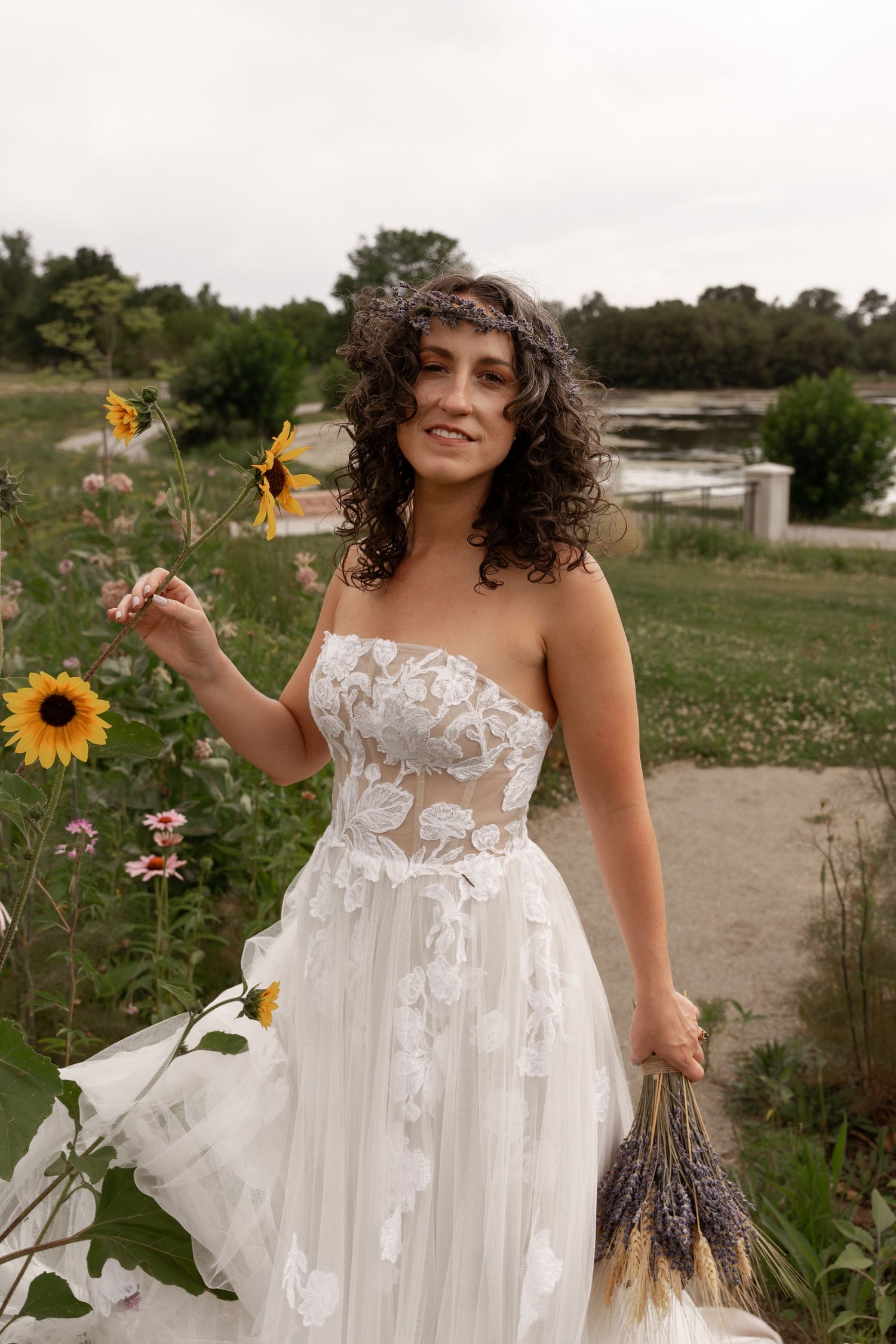 A white lace wedding dress flows elegantly in a field of sunflowers and wildflowers on a summer day.