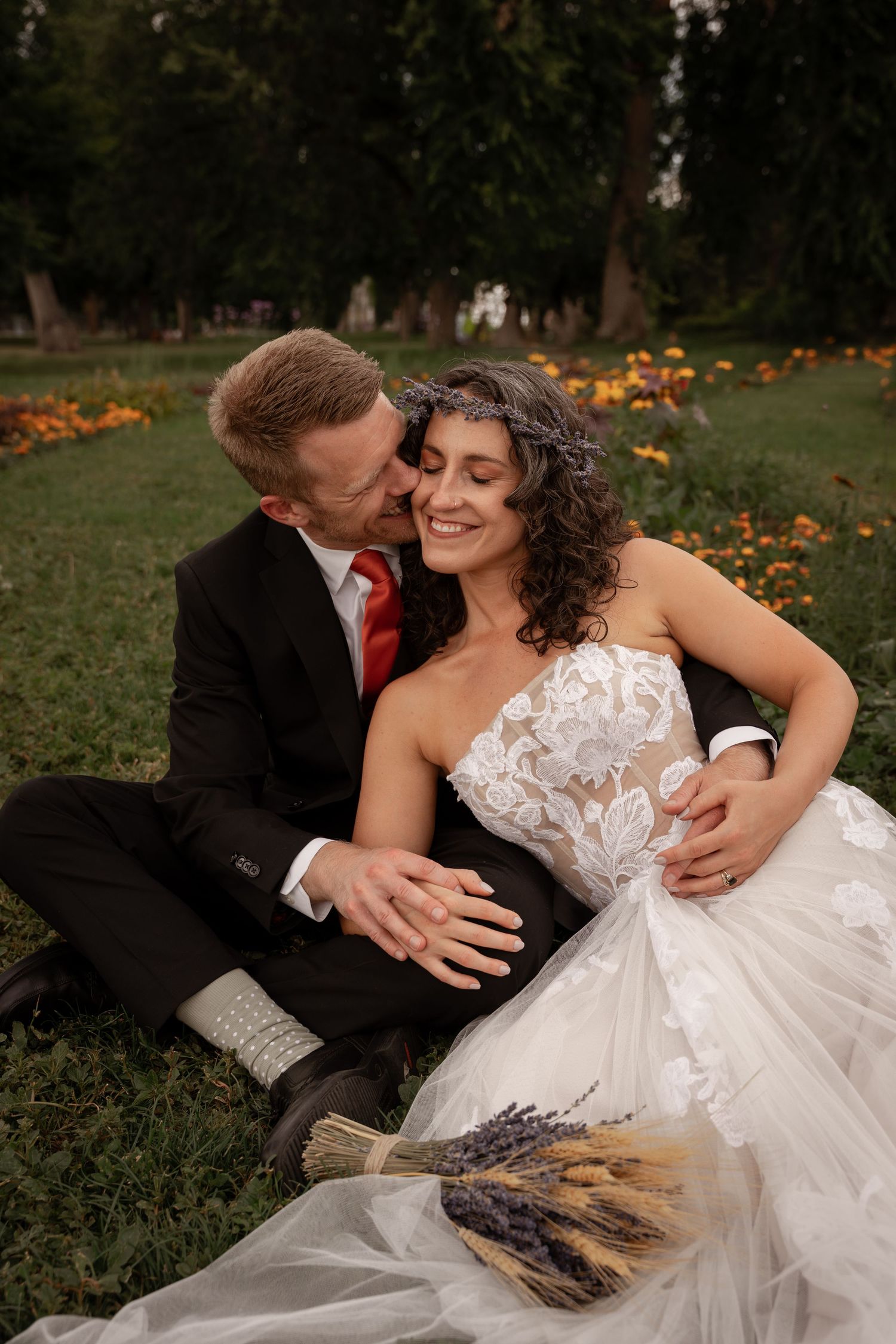 A romantic wedding couple embraces on the grass surrounded by orange flowers in a garden setting.
