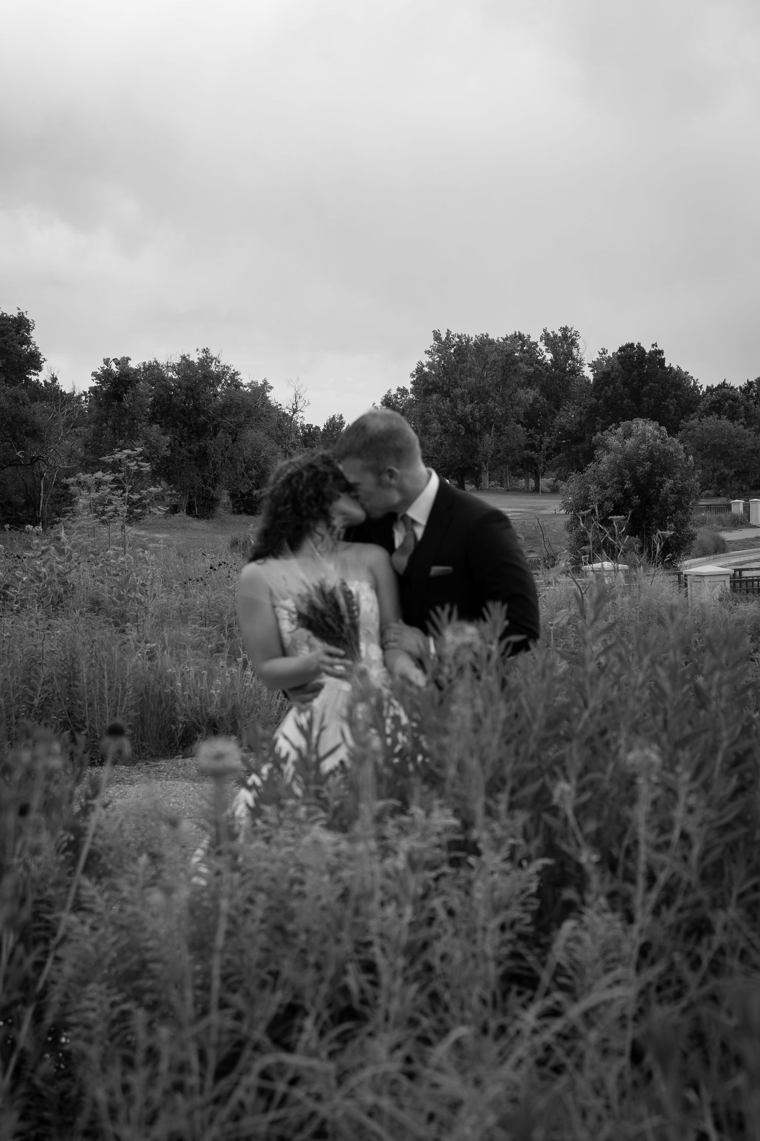 A sequence of black and white photos showing two people embracing in a field of tall grass and wildflowers.