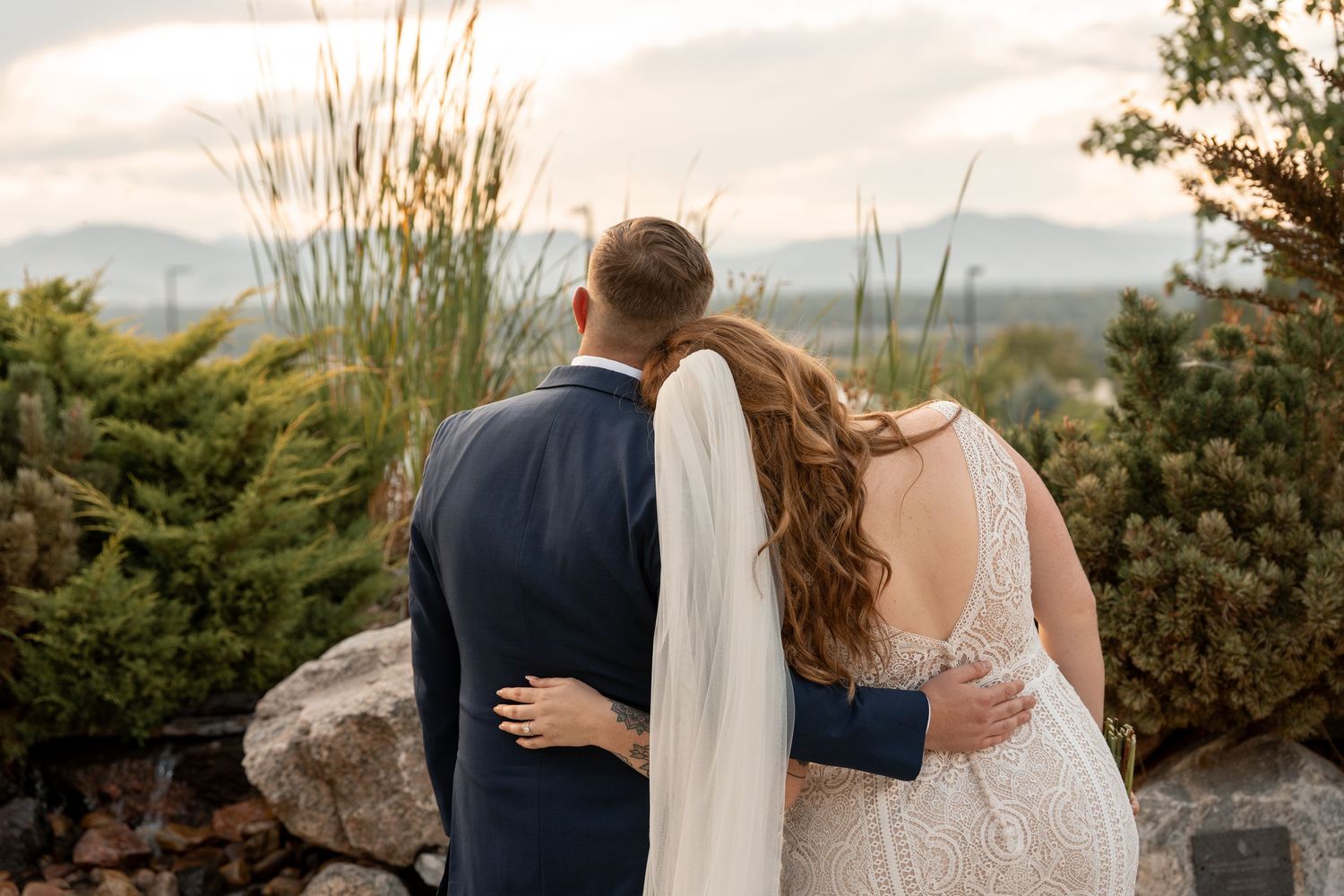 A romantic wedding couple embraces against a scenic mountain backdrop at sunset.