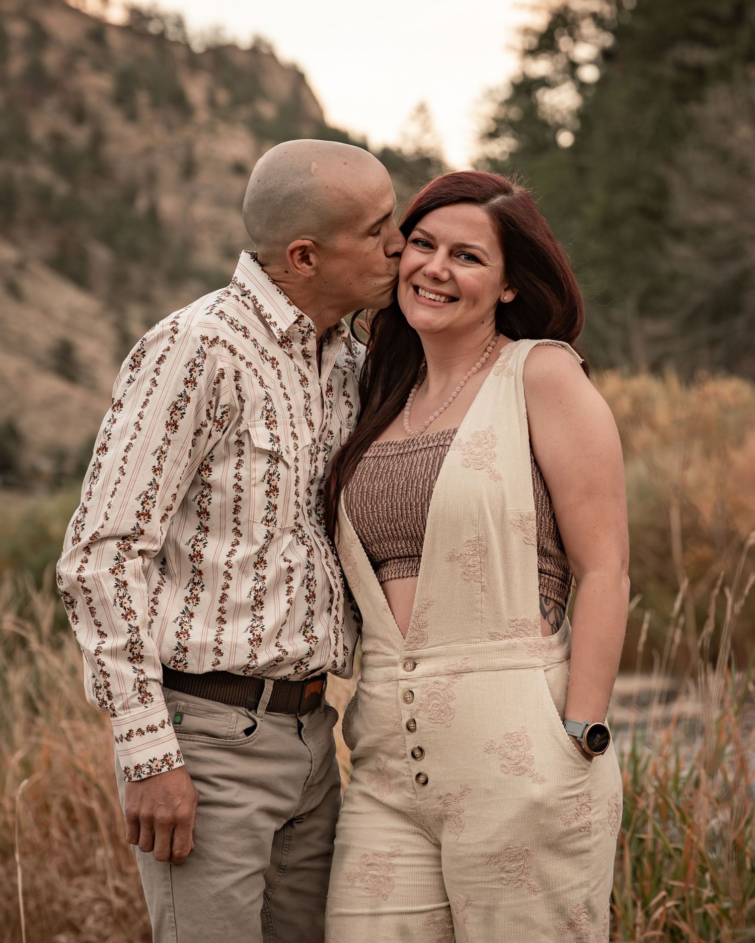 Romantic outdoor photoshoot in rustic outfits against a mountainous backdrop at sunset.