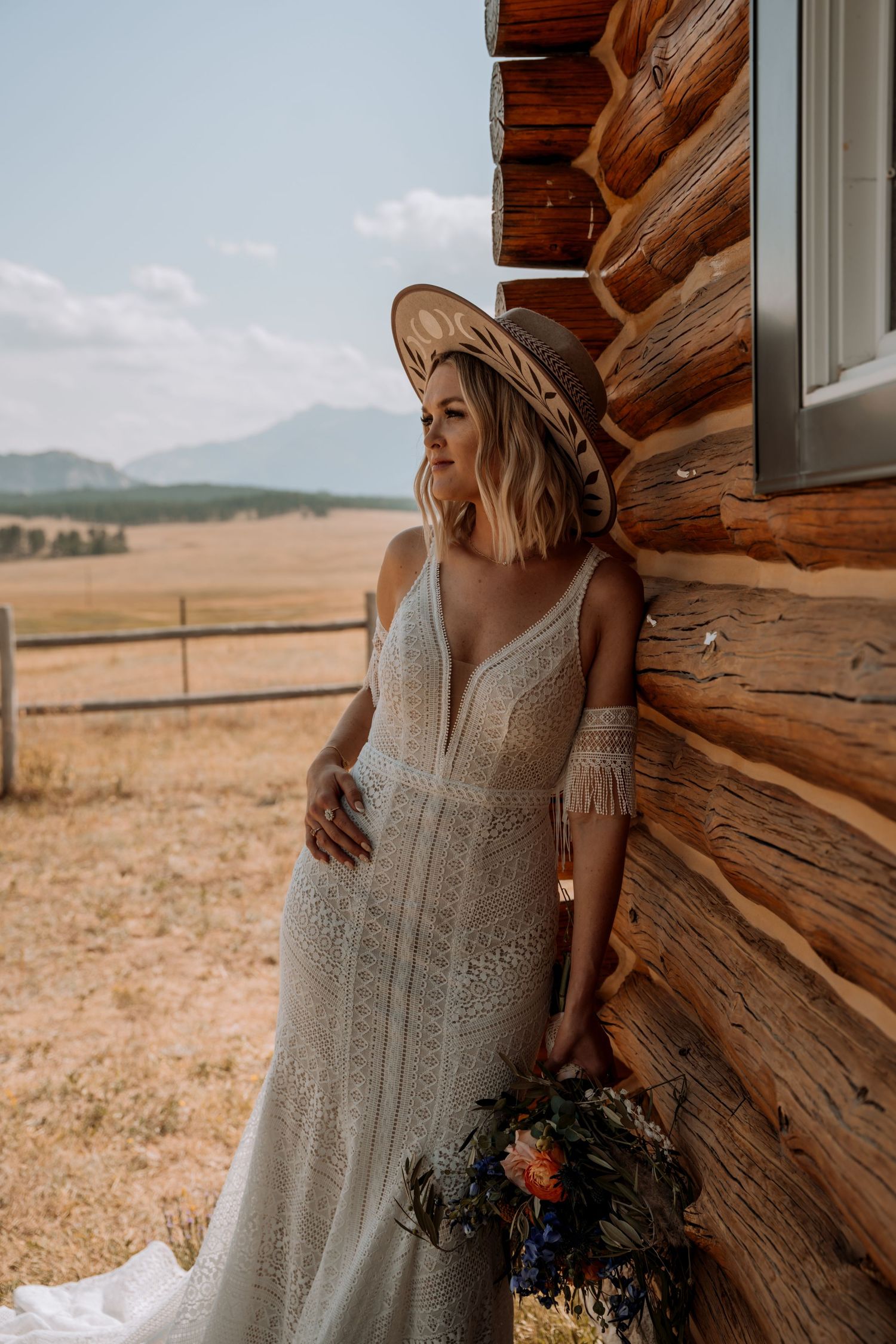 A rustic log cabin wedding scene with a bride in a vintage lace dress against a backdrop of golden prairie fields.