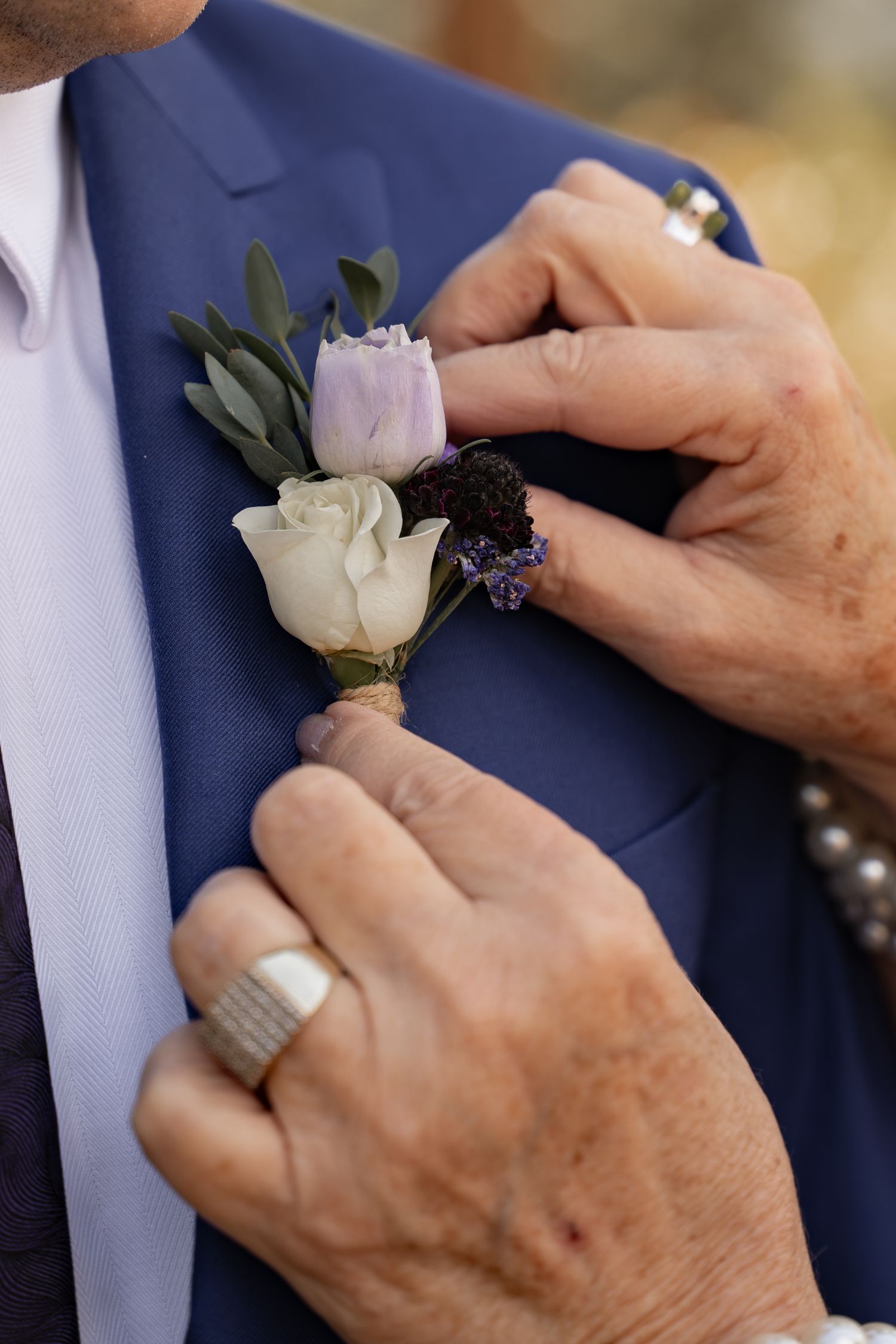 Close up of a woman's hands pinning a boutonniere onto a groom's lapel.