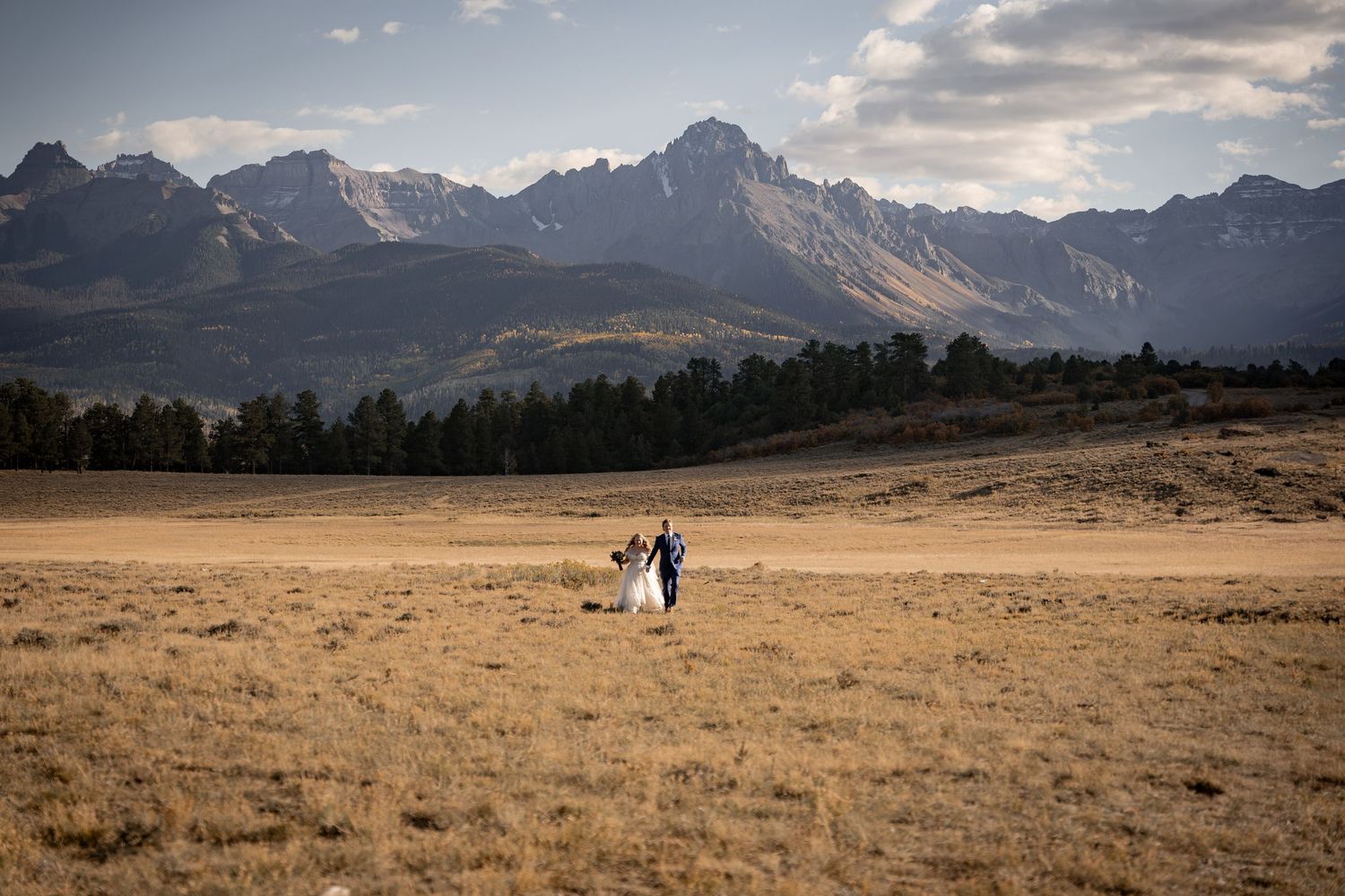 Dramatic mountain landscape with couple silhouetted in distance on golden plains.