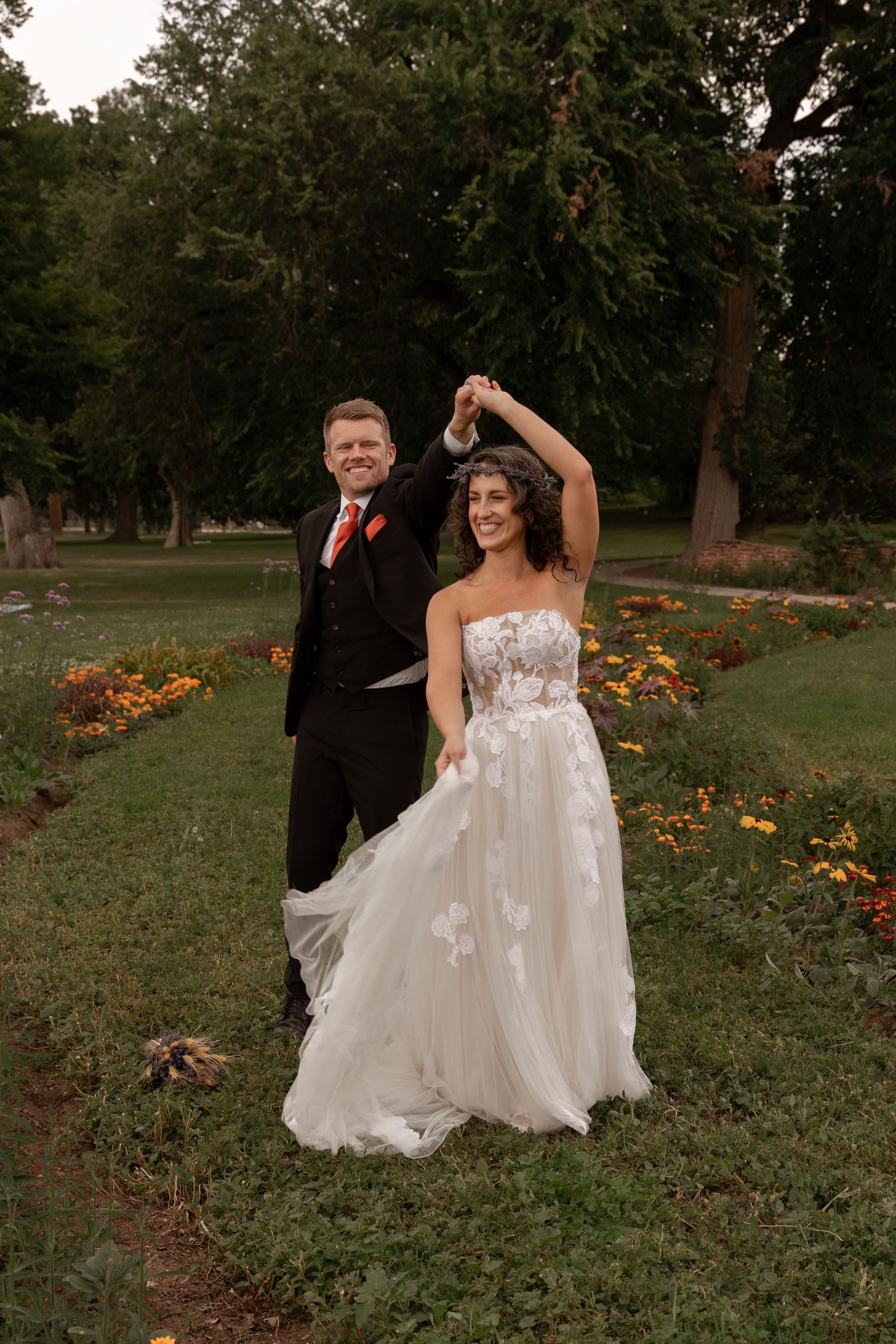 A couple dances together in a garden setting with orange flowers and trees in the background during their wedding celebration.