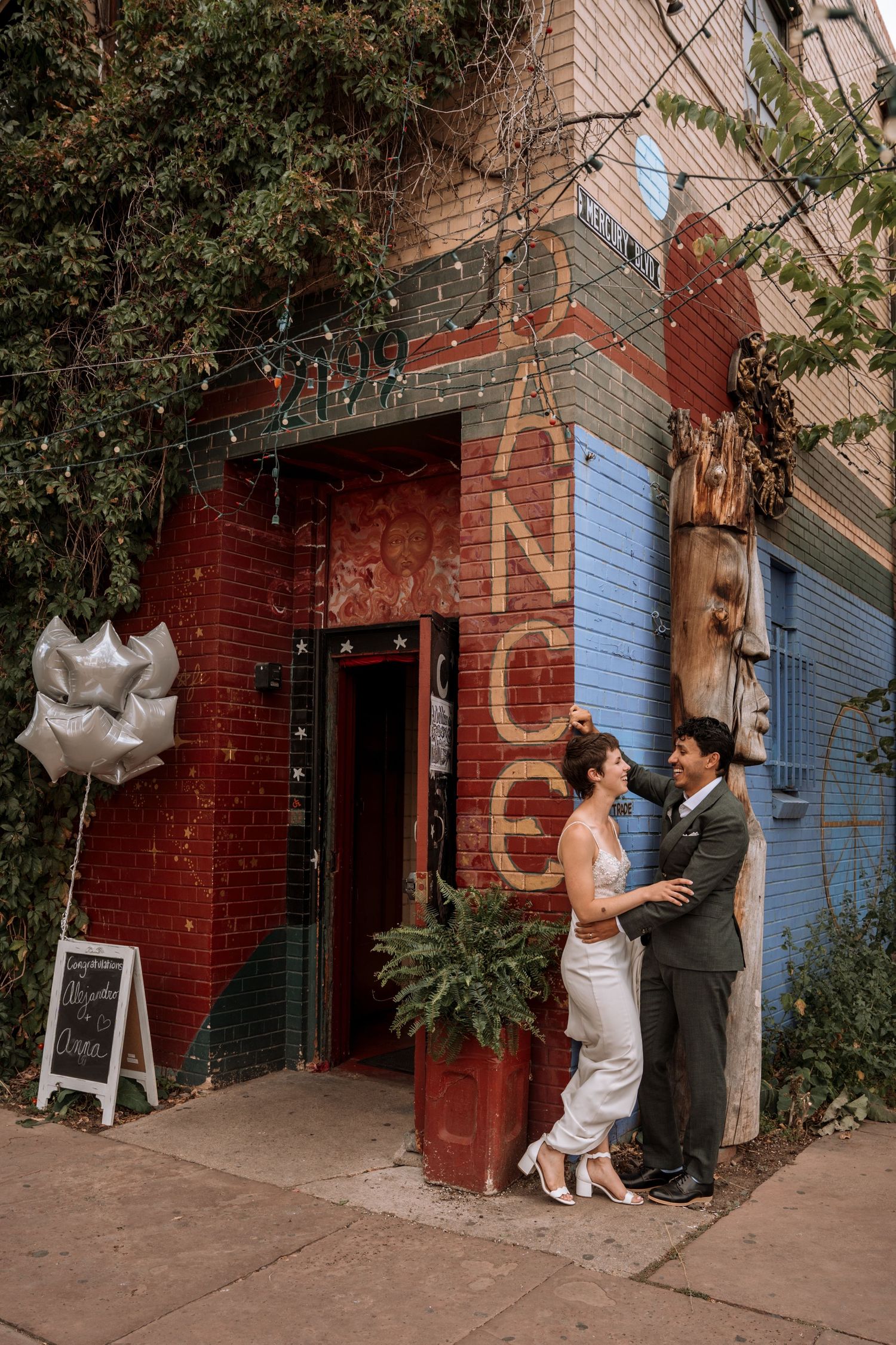 A romantic wedding couple shares intimate moments in a rustic brick alleyway with blue accents and white chairs.