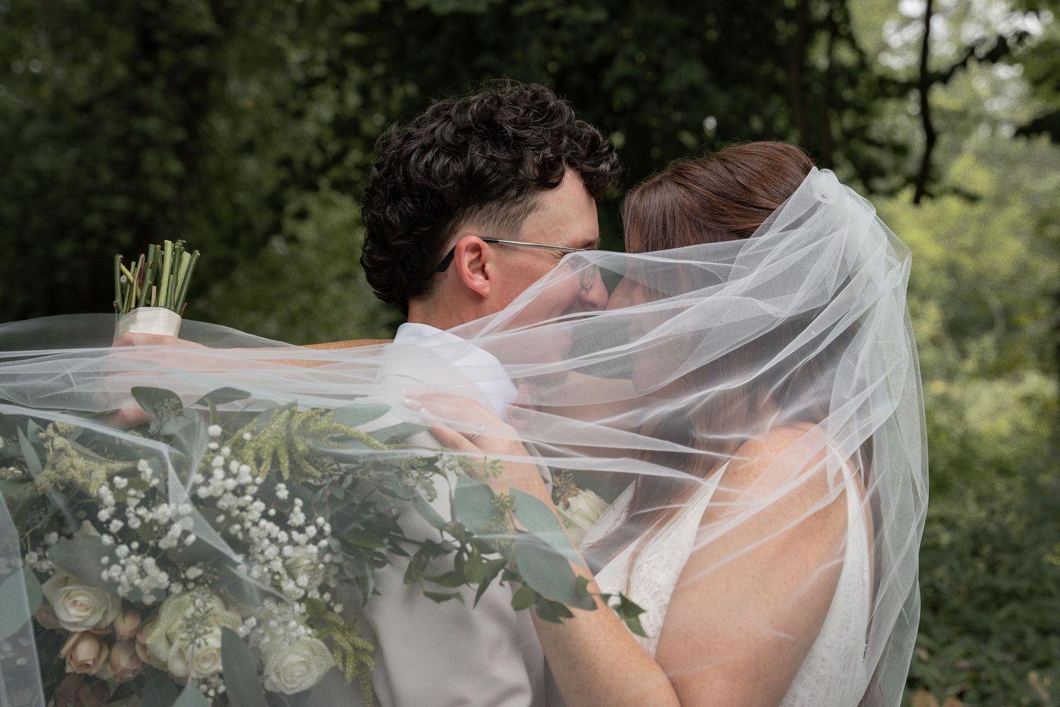 Romantic wedding portrait with flowing veil and natural greenery in background.