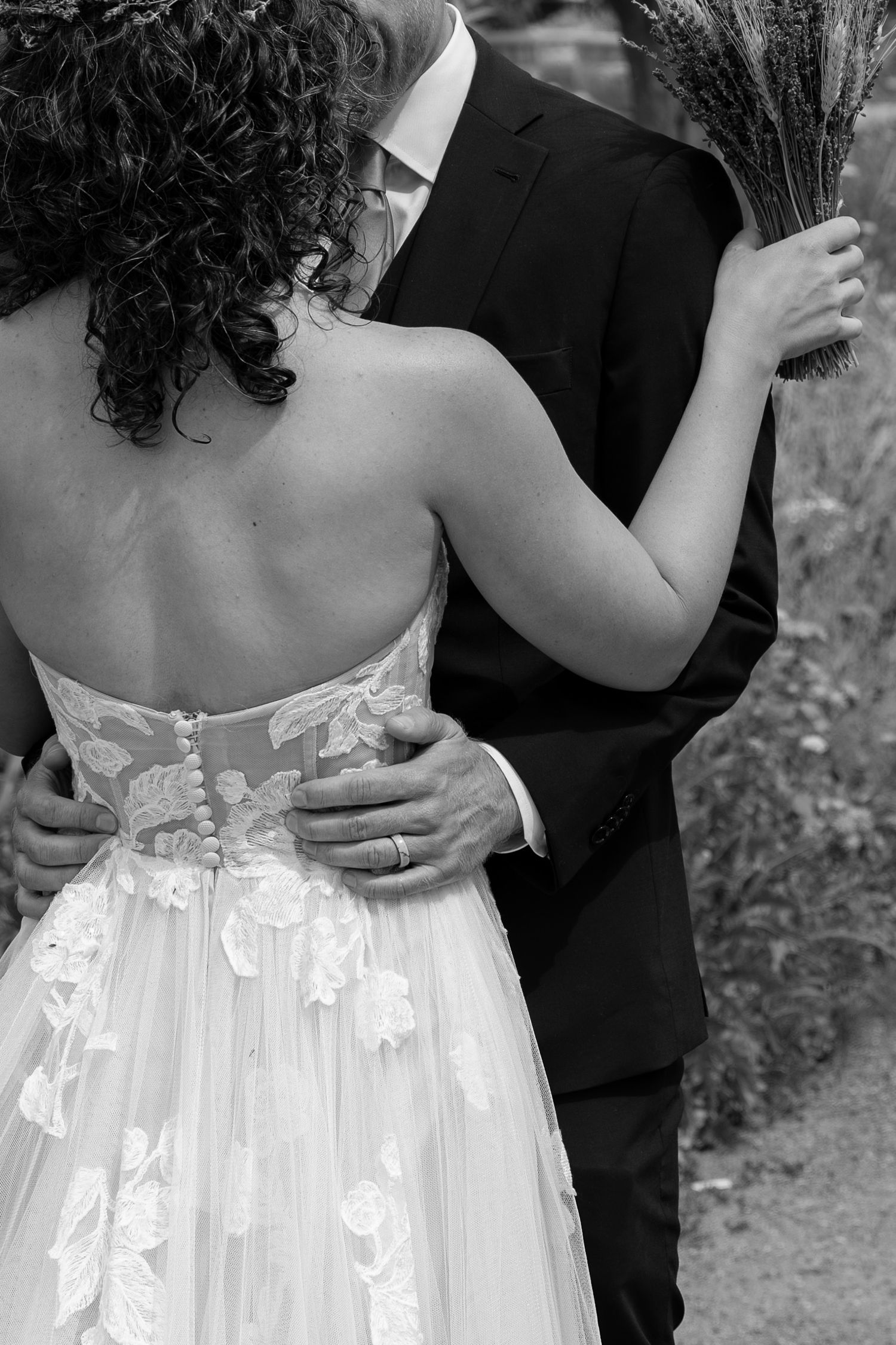 Black and white wedding photo showing couple embracing, with bride in lace dress and groom in dark suit.