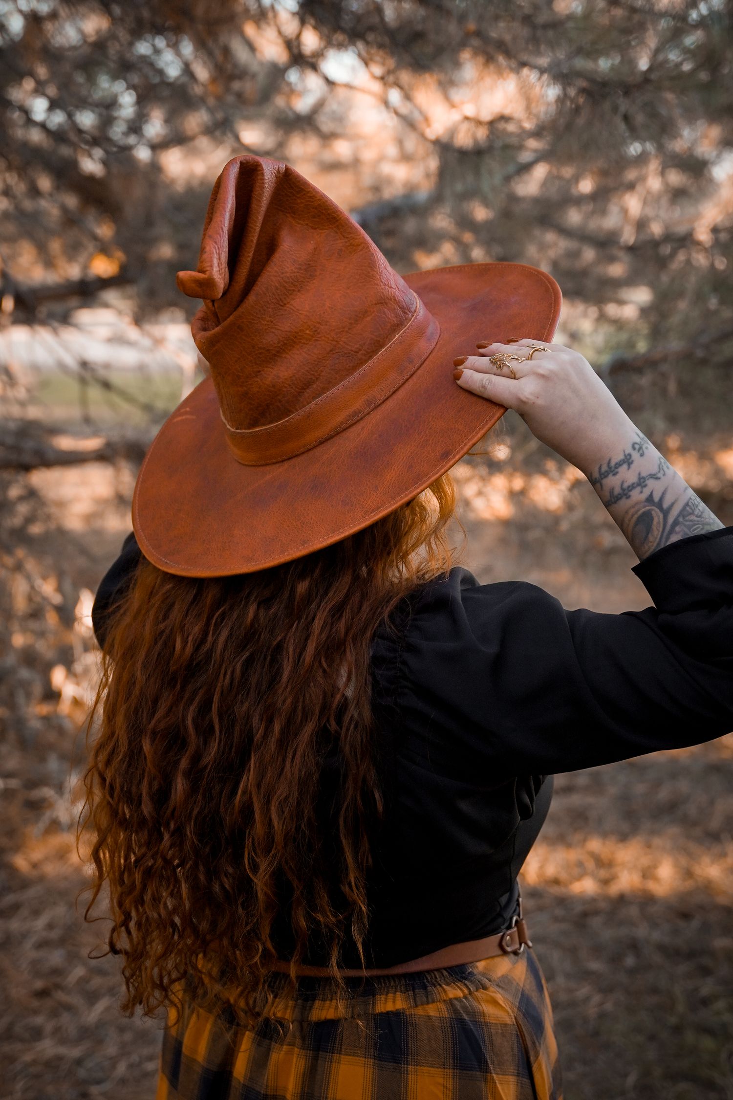 Autumn outdoor portrait with brown fedora hat against sunset-lit pine trees.